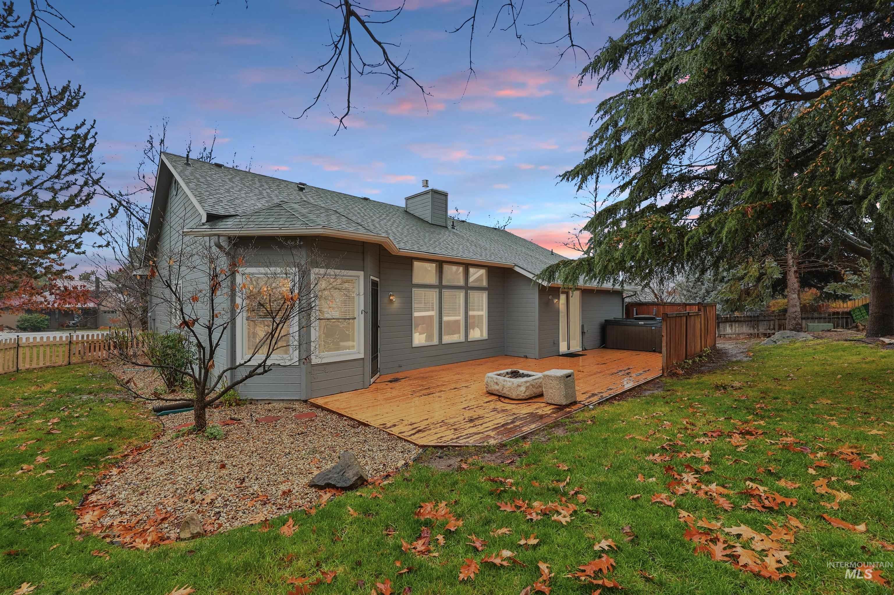 Back of property at dusk featuring a deck, a chimney, roof with shingles, and a jacuzzi