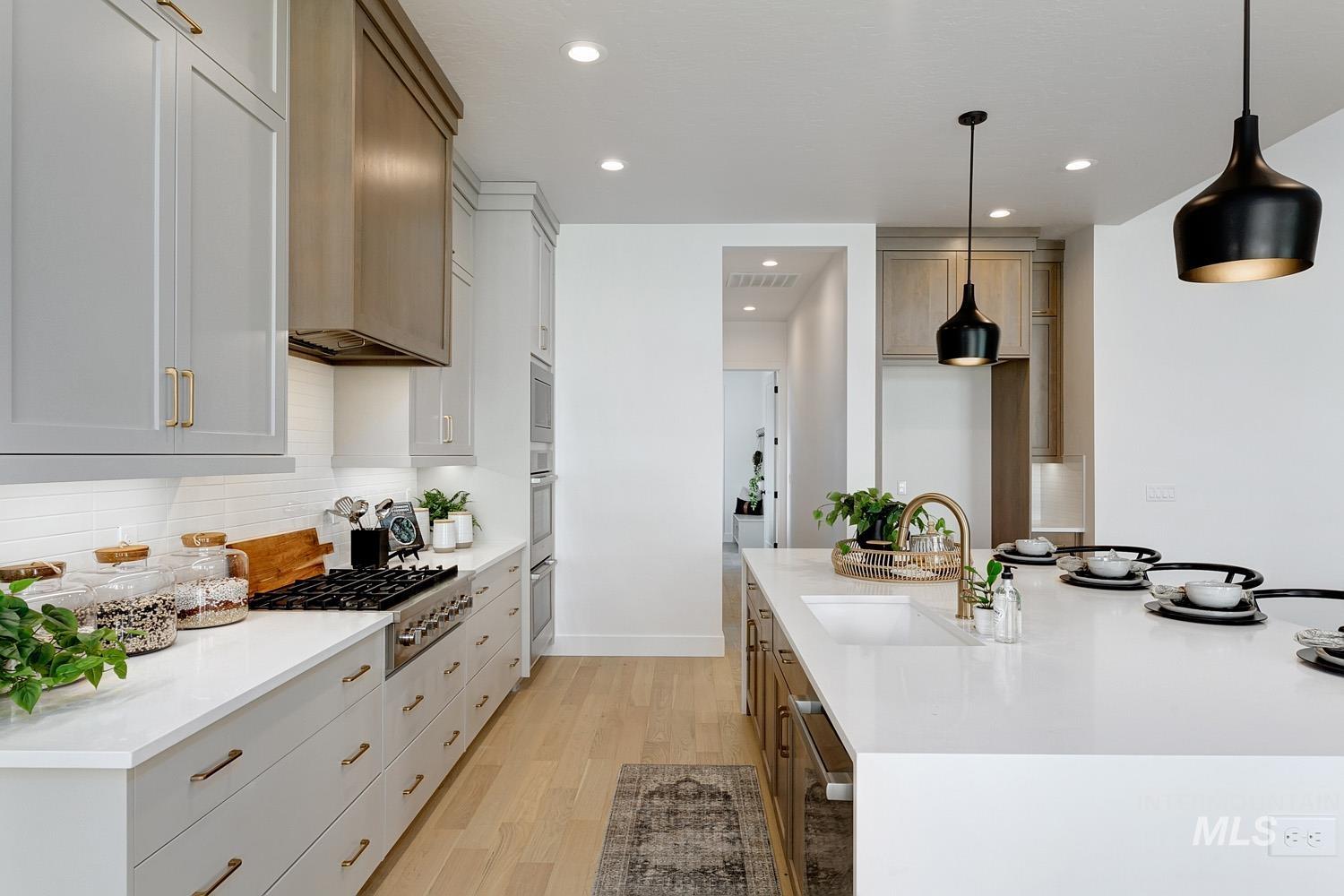 Kitchen with light wood finished floors, appliances with stainless steel finishes, light stone countertops, hanging light fixtures, and recessed lighting
