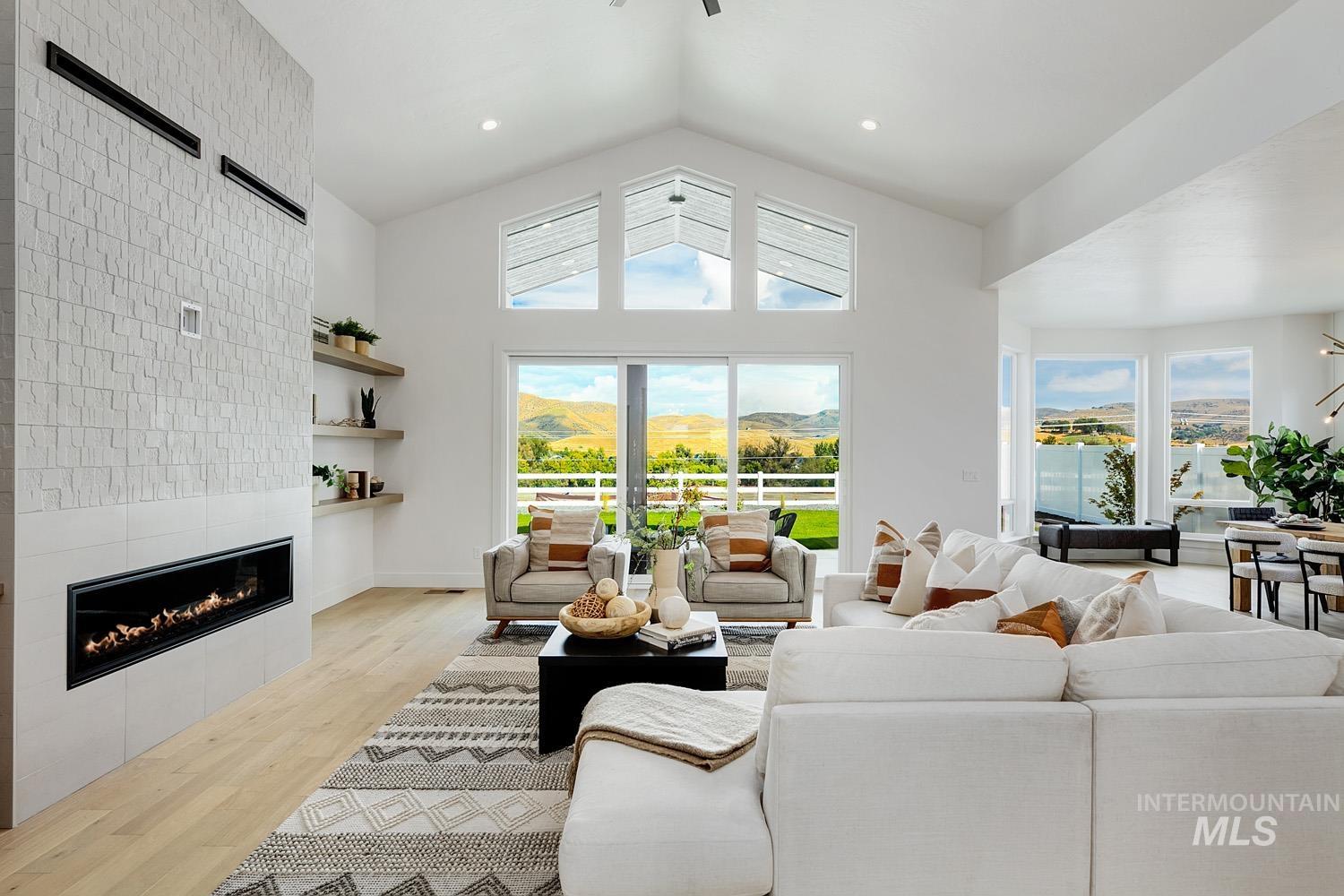 Living room with light wood-style flooring, healthy amount of natural light, a tile fireplace, a mountain view, and high vaulted ceiling