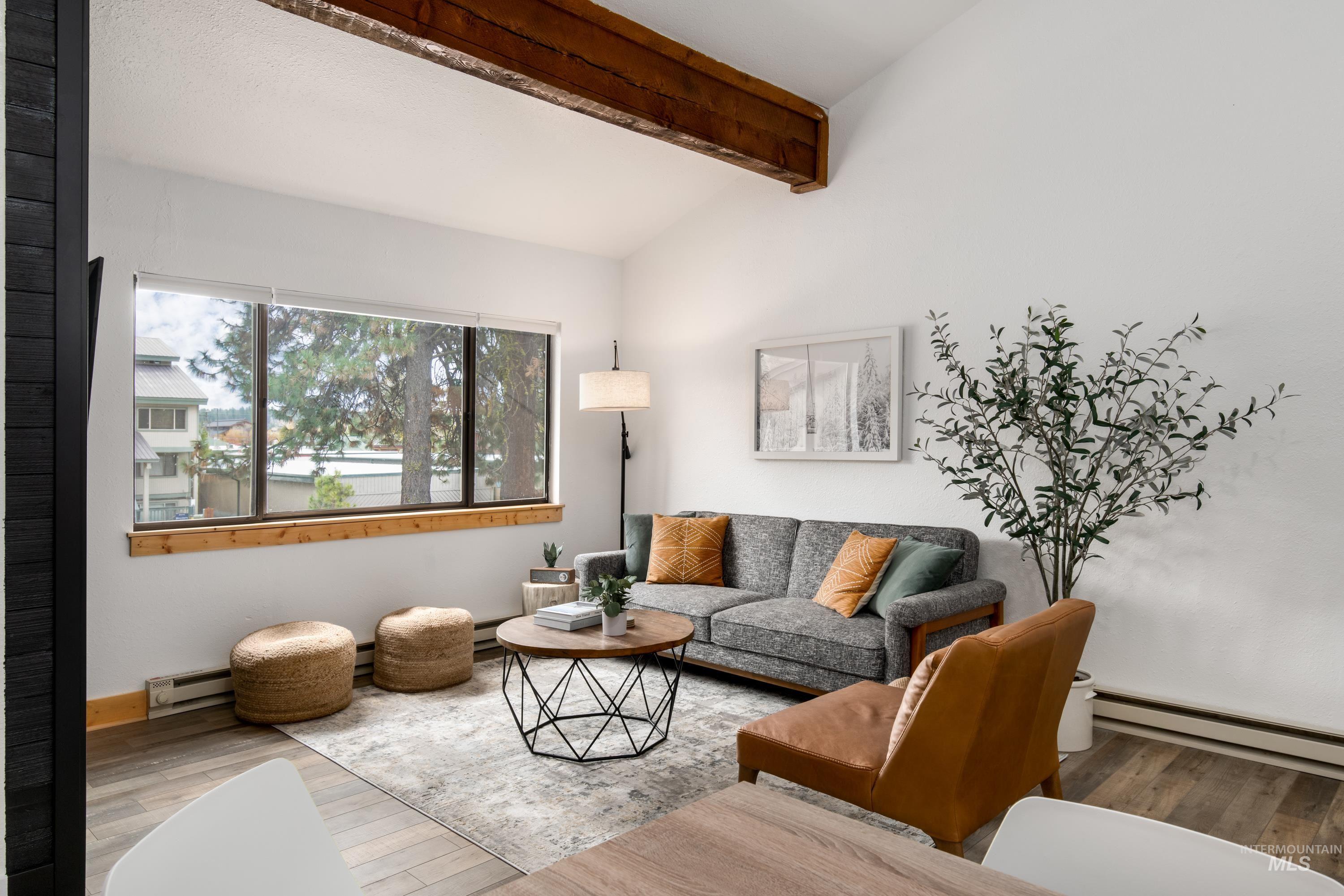 Open-concept living area featuring a vaulted ceiling with exposed wood beams, wood-finish flooring, and a large picture window