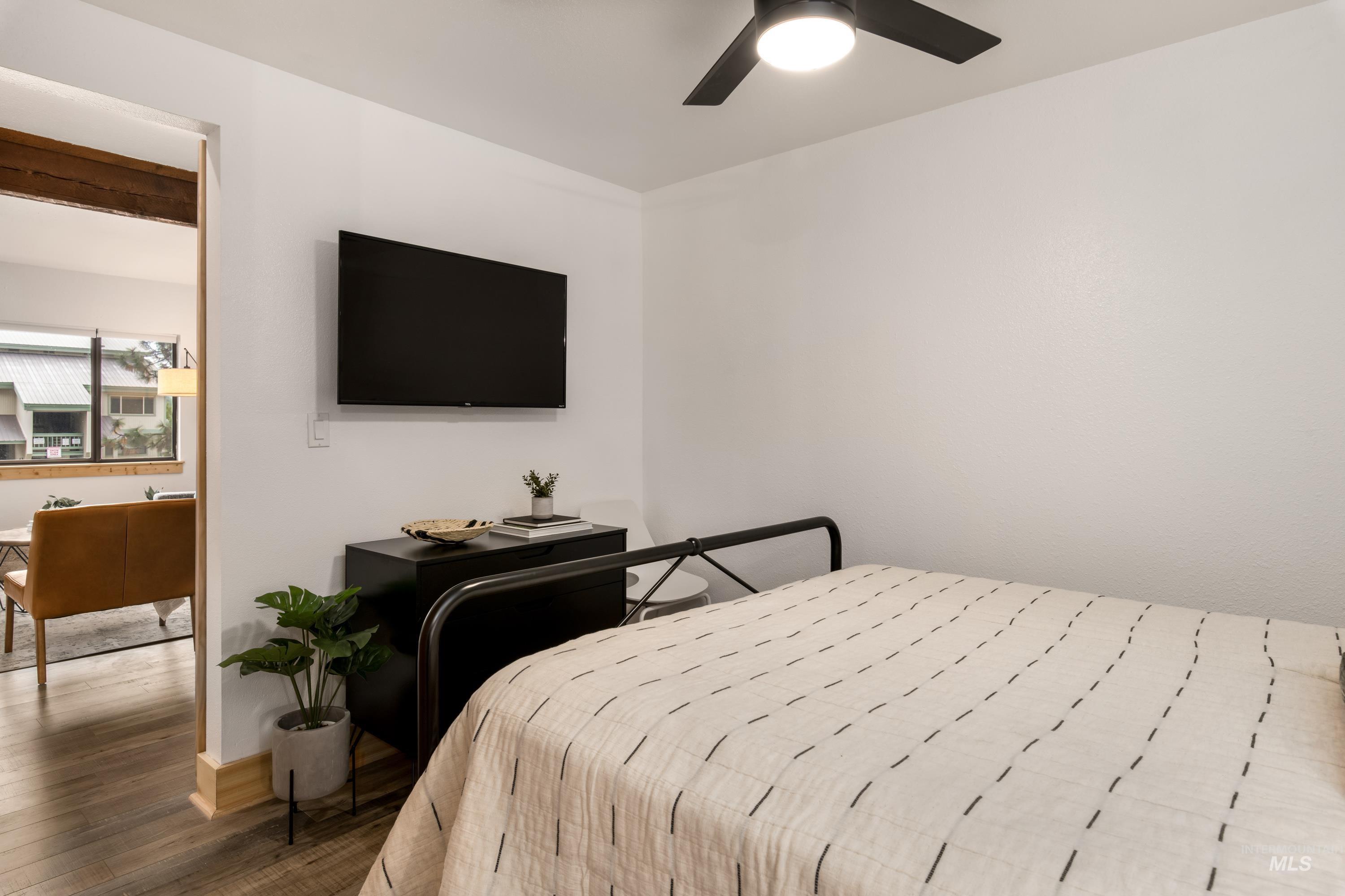 Bedroom with a ceiling fan, wall-mounted television, and wood-finish flooring extending into the adjacent room