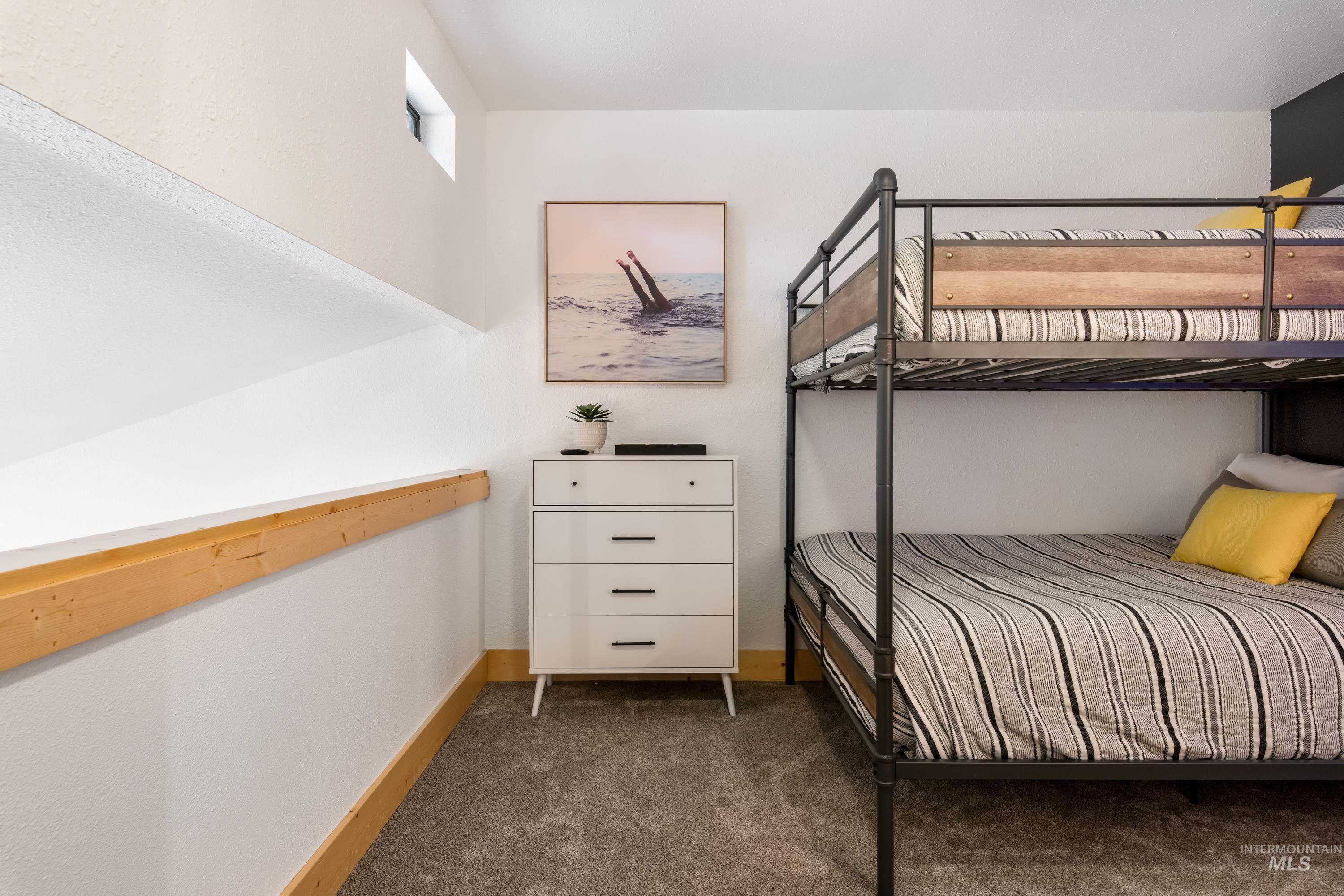 Carpeted room featuring a metal-frame bunk bed with wood-grain accents, a white dresser with black drawer pulls, and a horizontal window