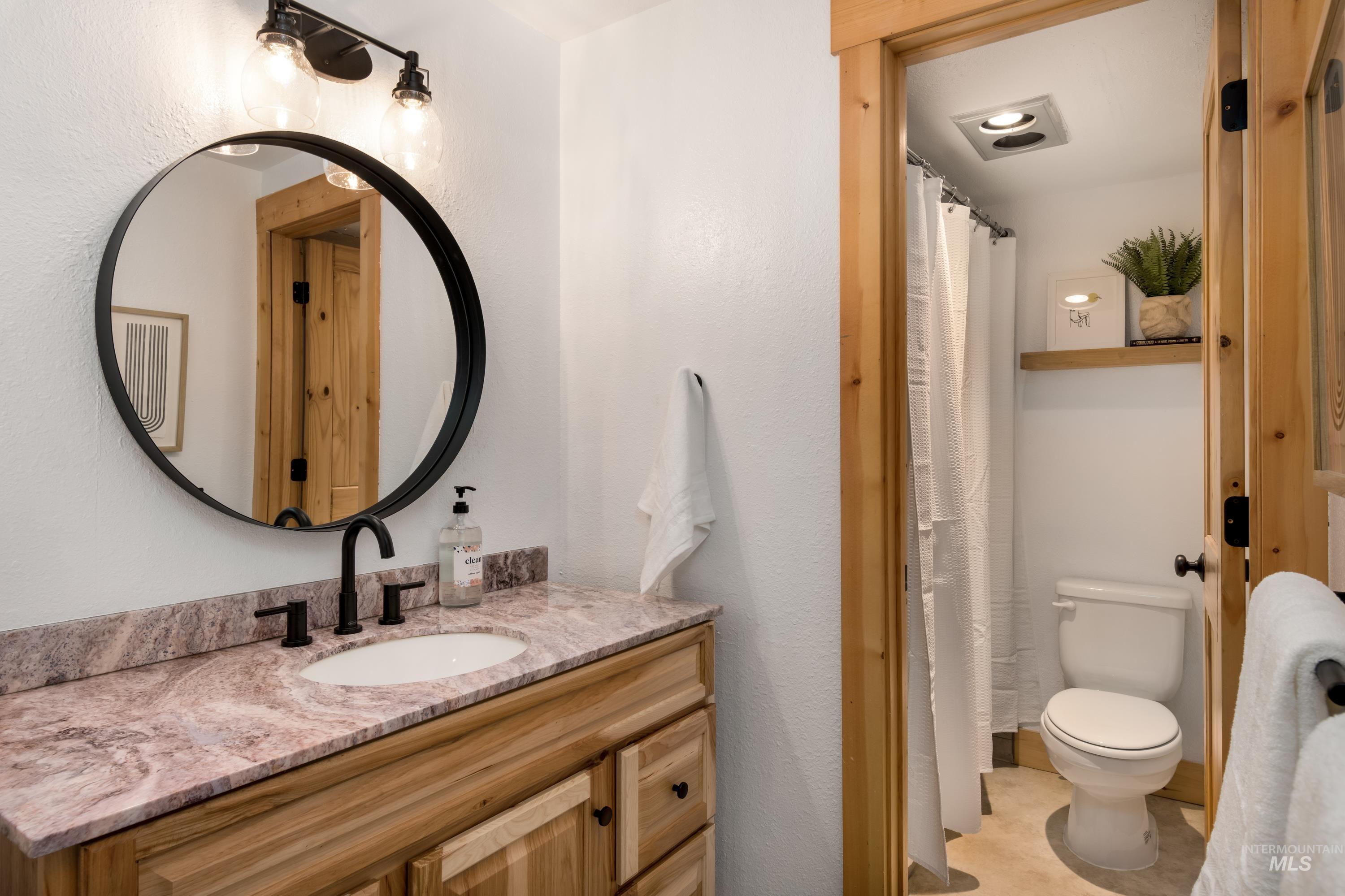 Bathroom vanity featuring a wood-finish cabinet, patterned countertop, and a circular black-framed mirror