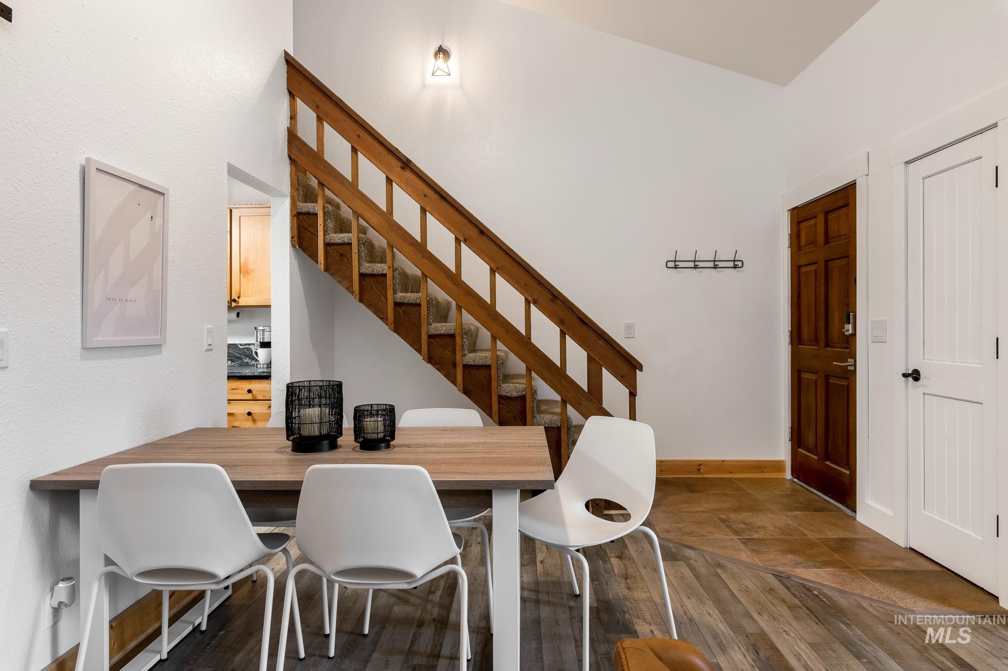Vaulted ceiling living area featuring a wood-finish staircase with carpeted treads, a dark wood entry door, white interior doors, and wood-finish flooring