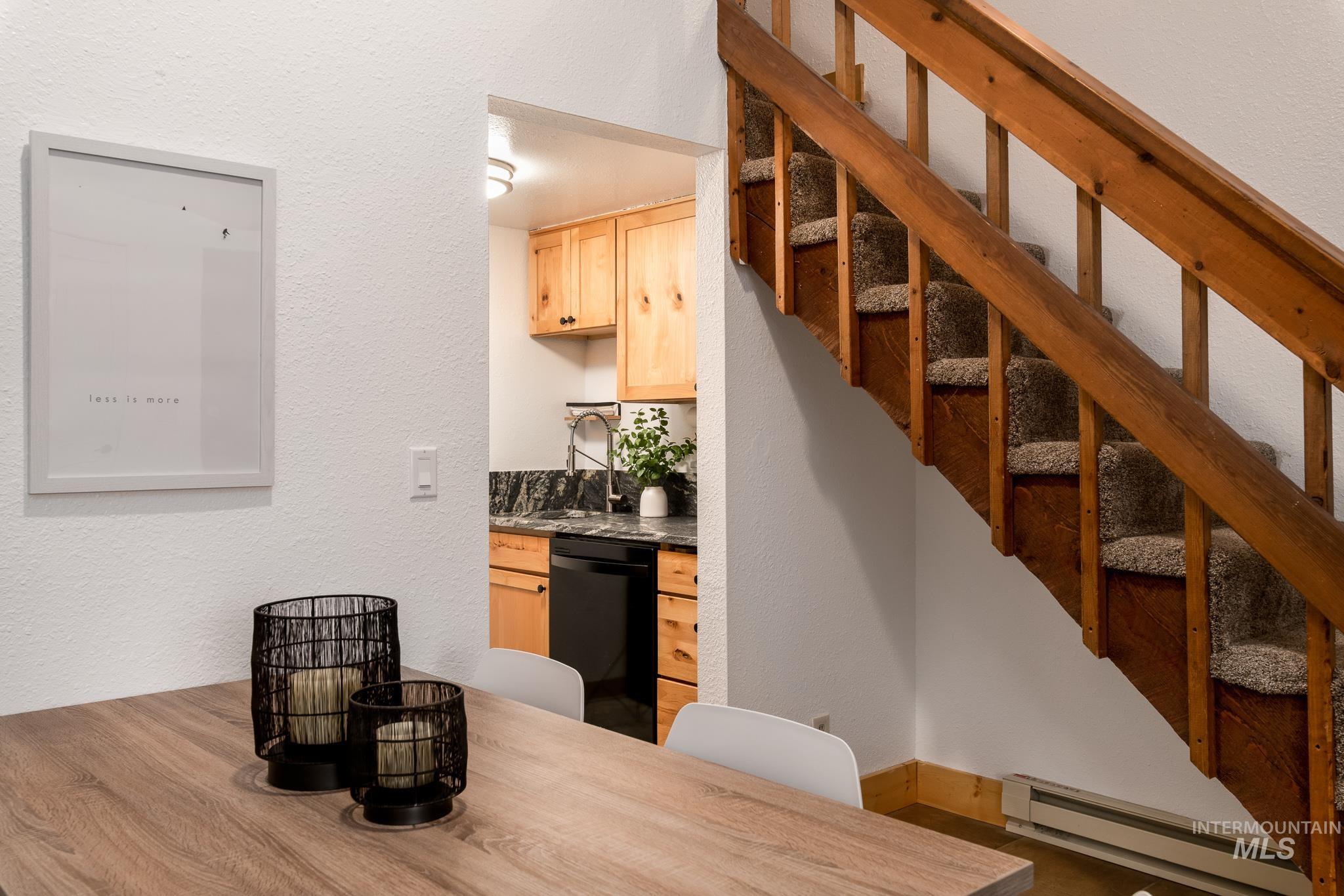 Carpeted staircase with wood railings, positioned beside a kitchen featuring light wood cabinetry, a dark countertop, and a black appliance
