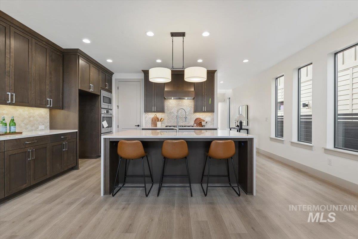 Kitchen featuring a breakfast bar area, light stone countertops, decorative light fixtures, dark wood finish cabinets, and a center island with sink