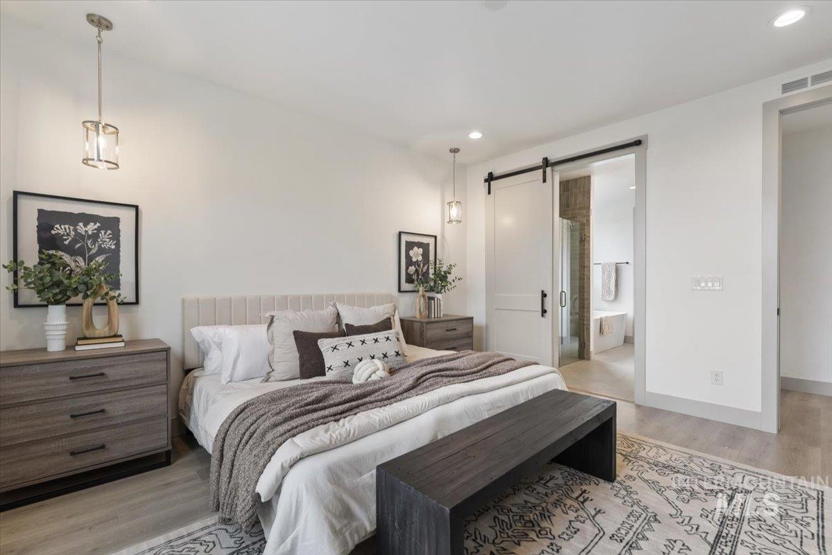 Bedroom with a barn door, light wood-type flooring, recessed lighting, and ensuite bathroom