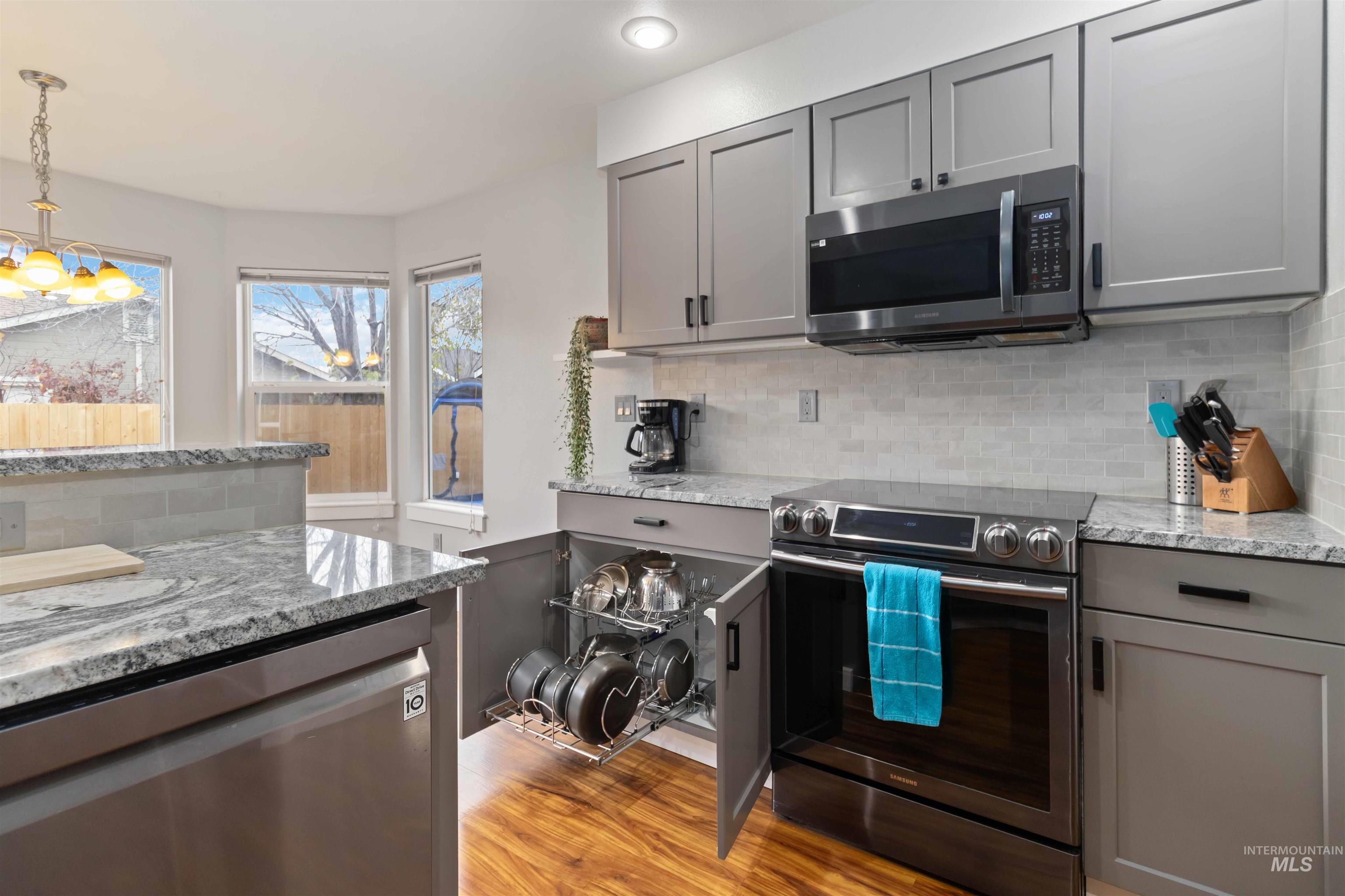 Kitchen featuring gray cabinetry, appliances with stainless steel finishes, light stone counters, backsplash, and light wood finished floors