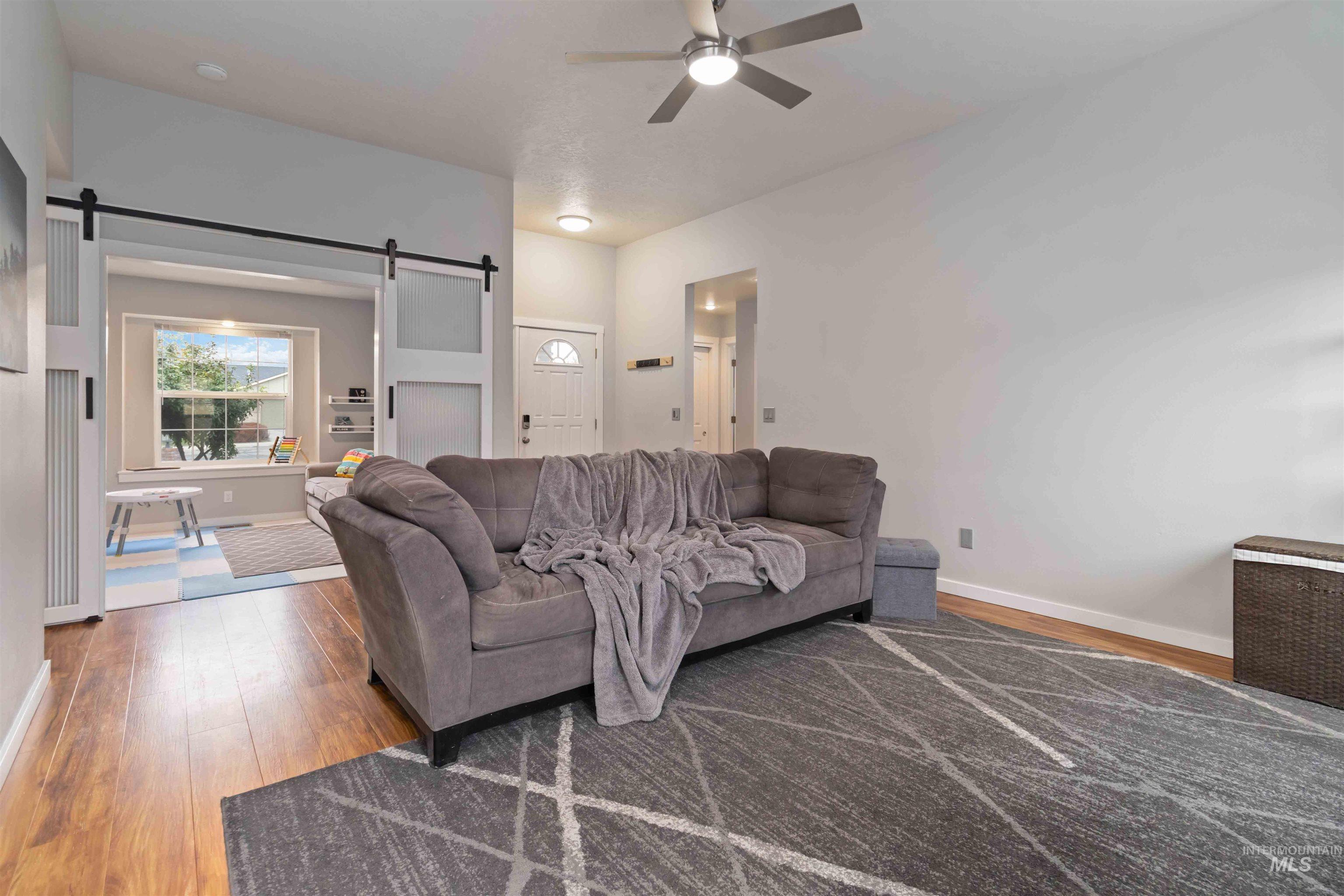 Living room featuring a barn door, light wood-style floors, and ceiling fan