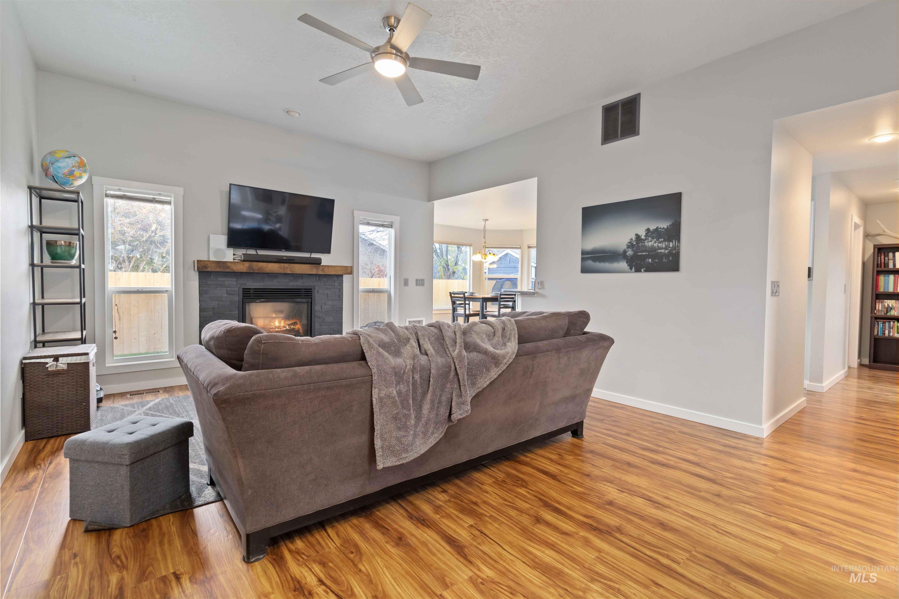 Living area with light wood-type flooring, a ceiling fan, and a glass covered fireplace
