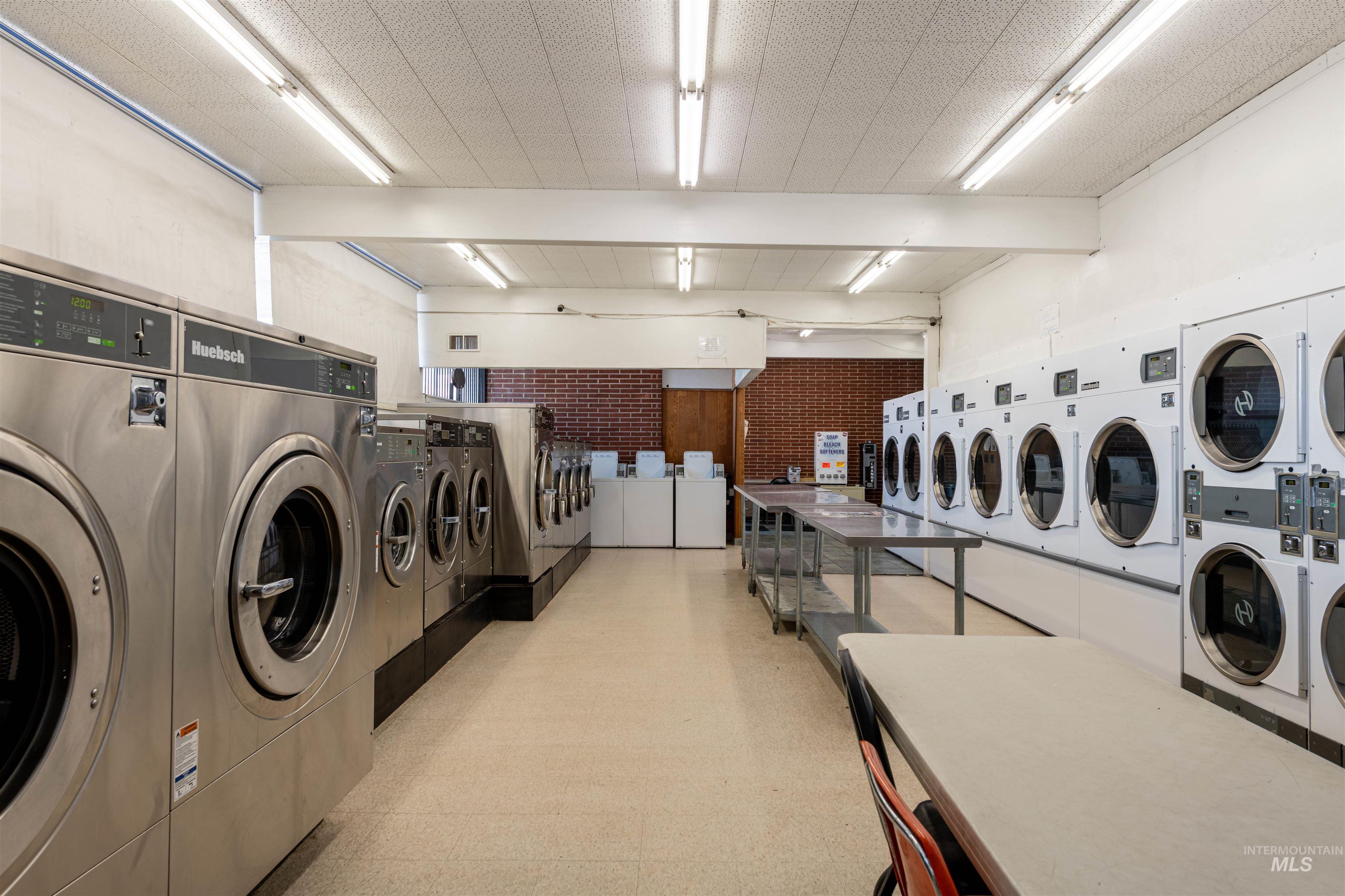 Shared laundry room with light flooring, washer and clothes dryer, and brick wall