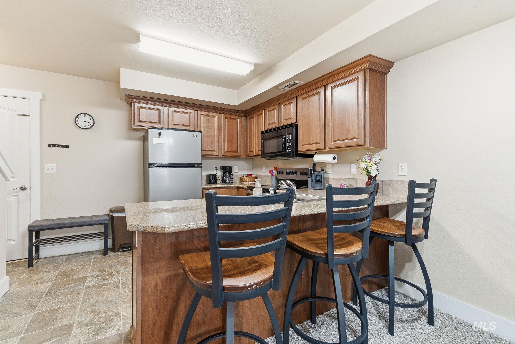 Kitchen featuring a breakfast bar, appliances with stainless steel finishes, a peninsula, brown cabinets, and light stone counters