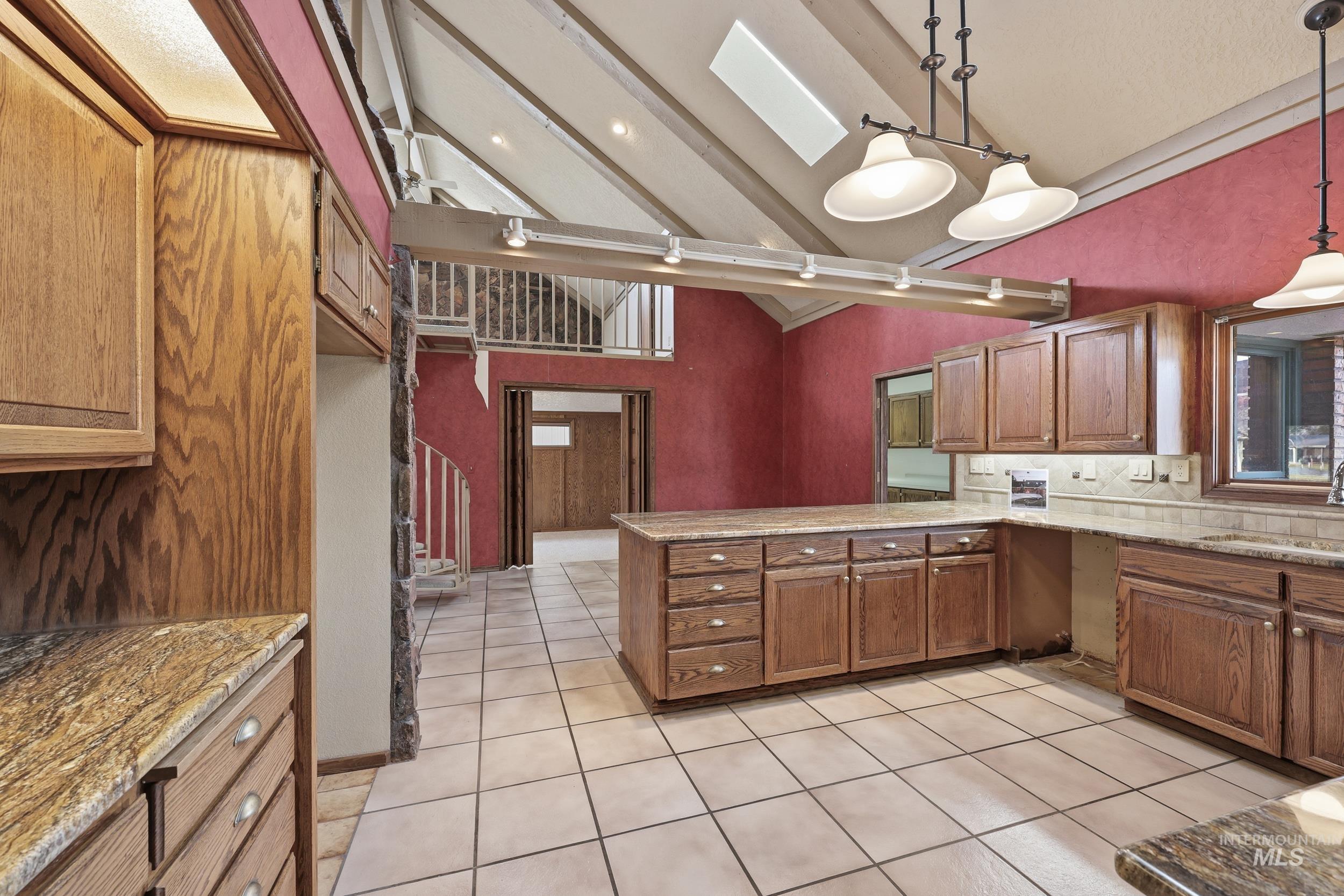 Kitchen with brown cabinetry, a skylight, pendant lighting, a peninsula, and high vaulted ceiling