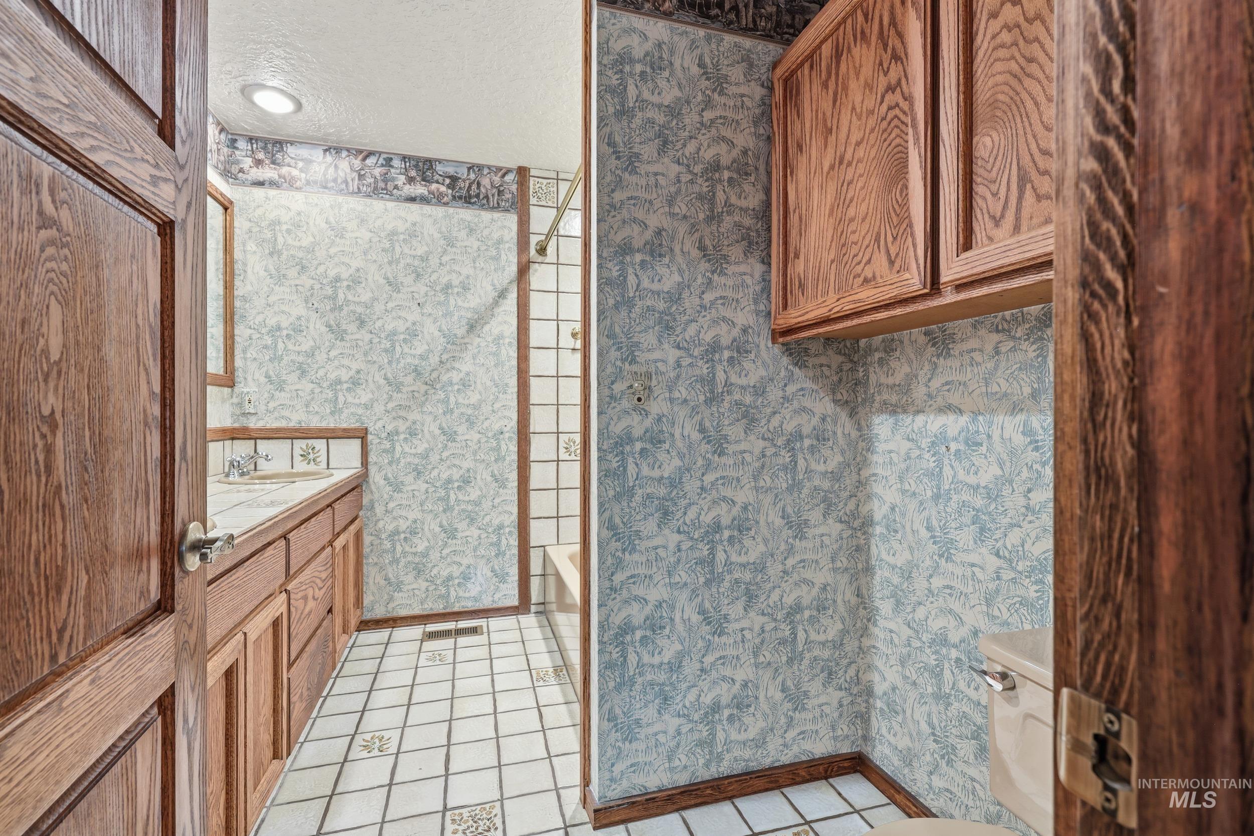 Full bath featuring wallpapered walls, vanity, a textured ceiling, light tile patterned floors, and washtub / shower combination