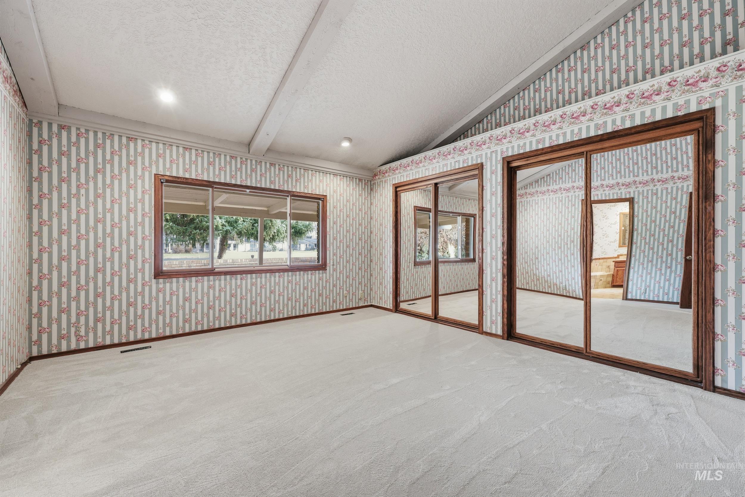 Unfurnished room featuring wallpapered walls, a textured ceiling, lofted ceiling, and carpet