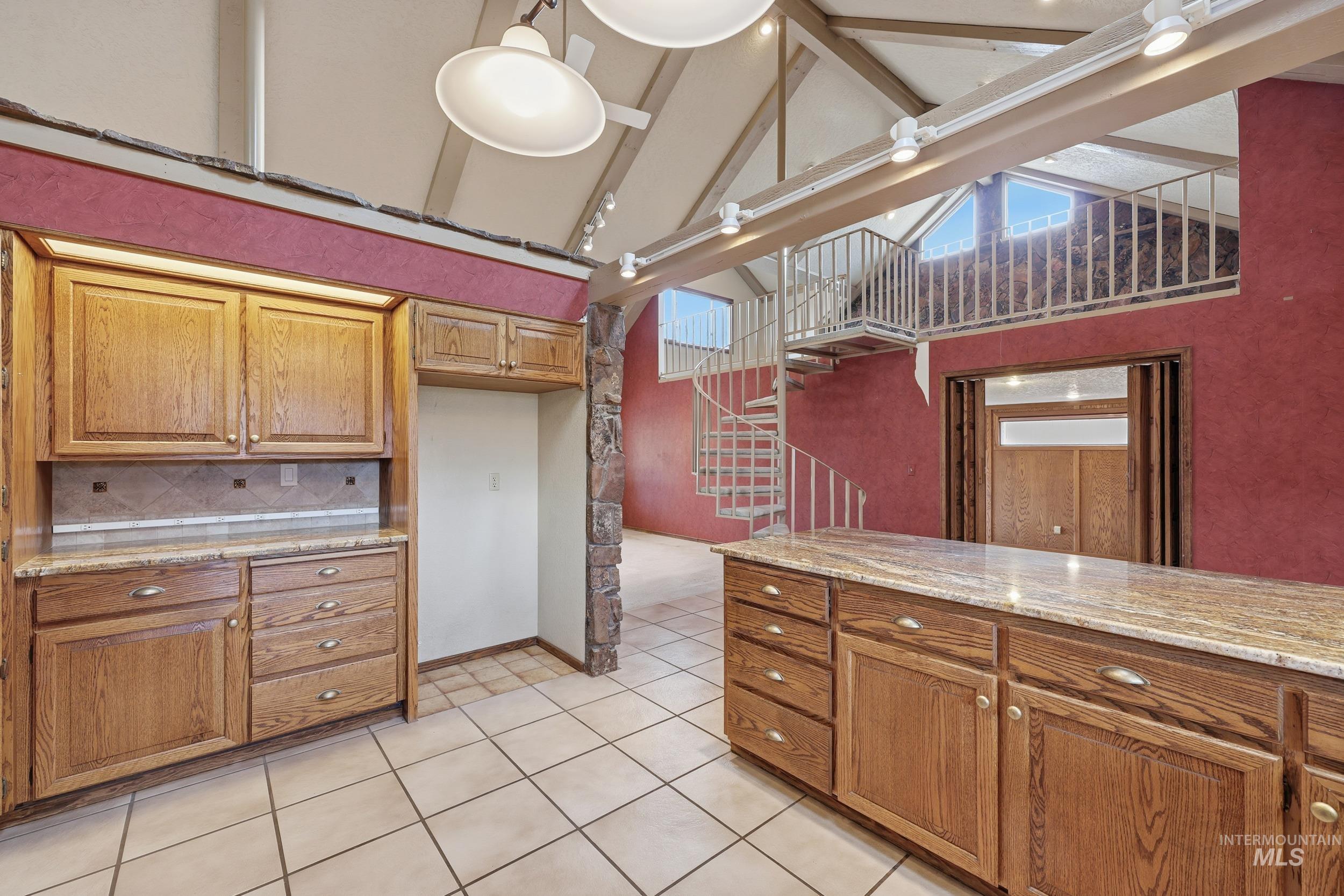 Kitchen with brown cabinets, light stone counters, beam ceiling, light tile patterned flooring, and high vaulted ceiling
