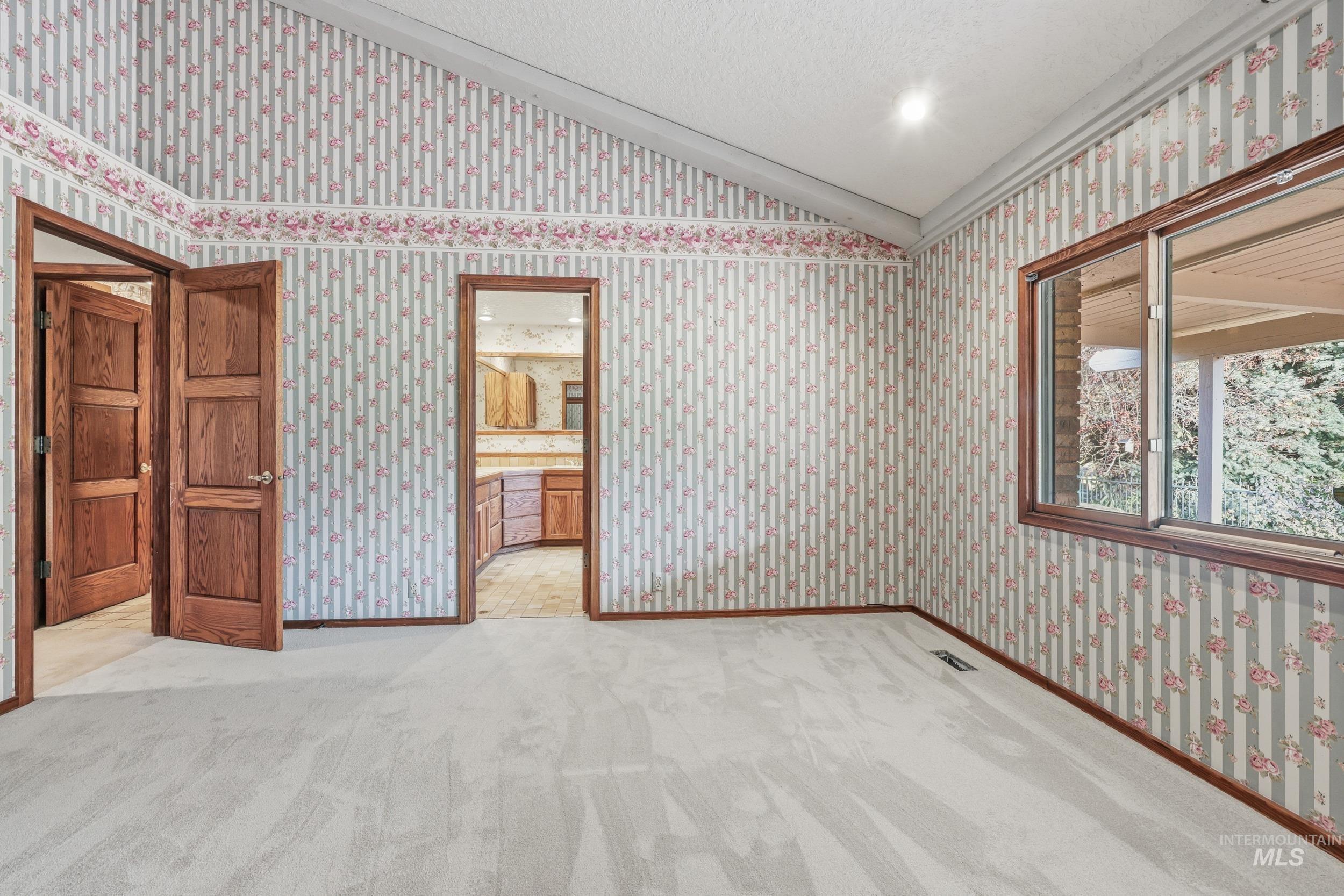 Unfurnished bedroom featuring lofted ceiling, wallpapered walls, carpet floors, and ensuite bathroom