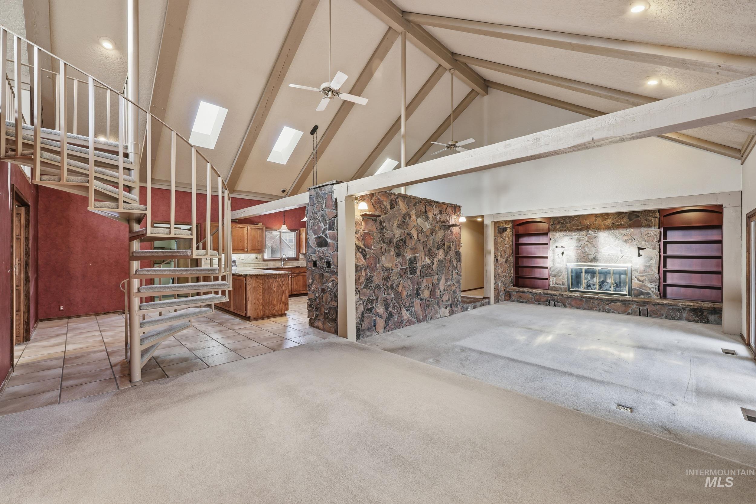 Unfurnished living room with high vaulted ceiling, a ceiling fan, beam ceiling, light carpet, and a skylight