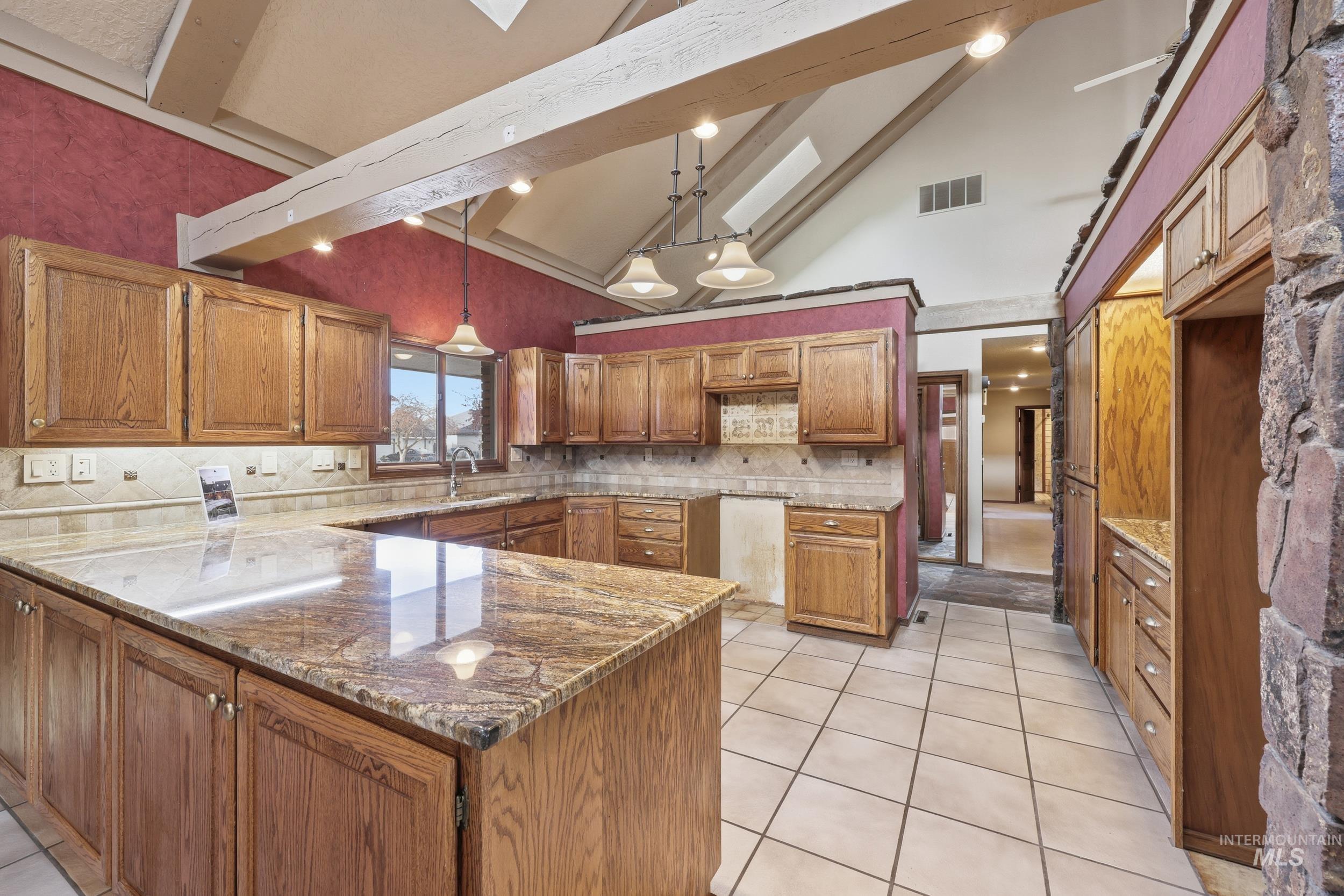 Kitchen with brown cabinets, high vaulted ceiling, dark stone countertops, pendant lighting, and a skylight
