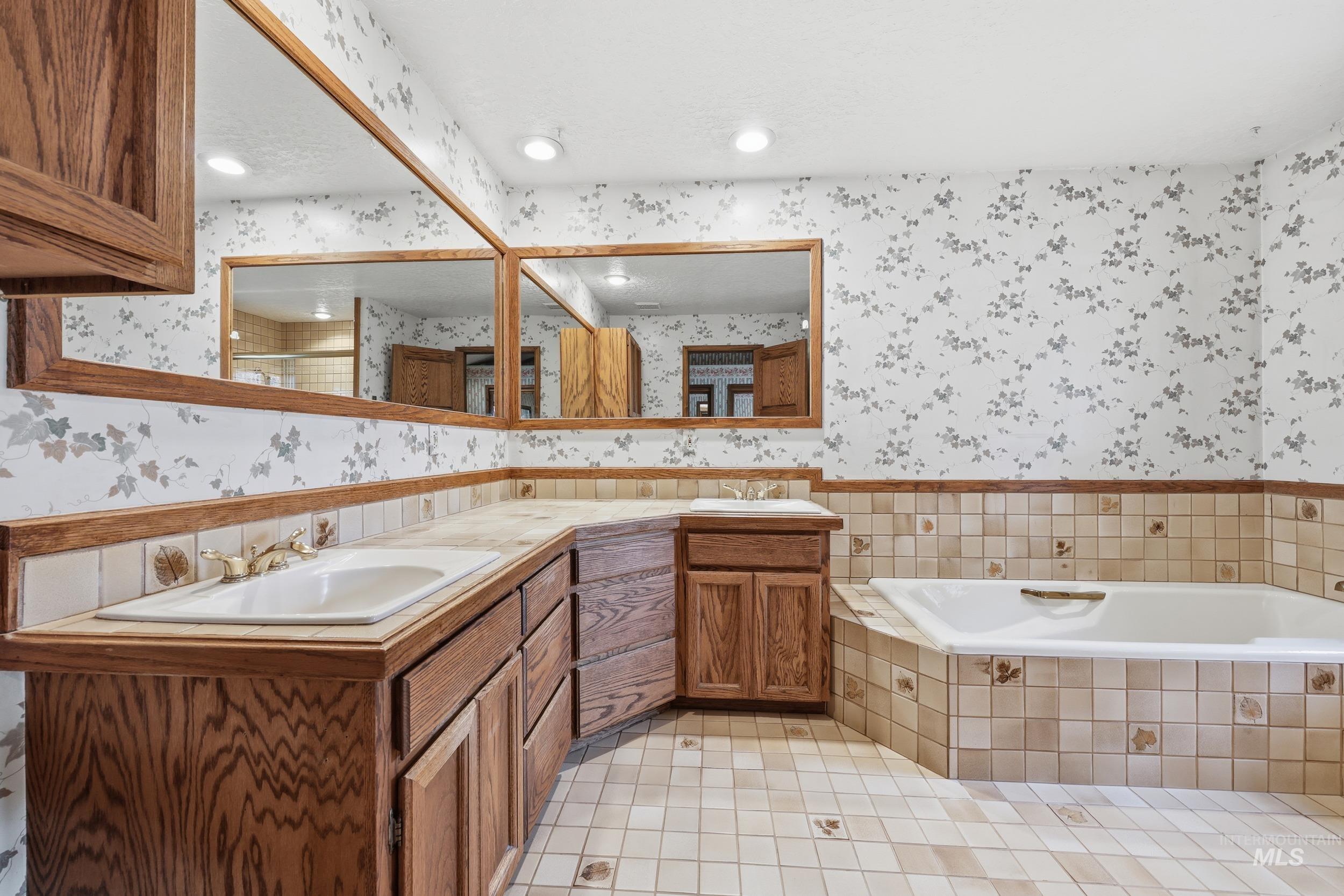 Full bathroom with wallpapered walls, double vanity, a garden tub, light tile patterned floors, and a wainscoted wall