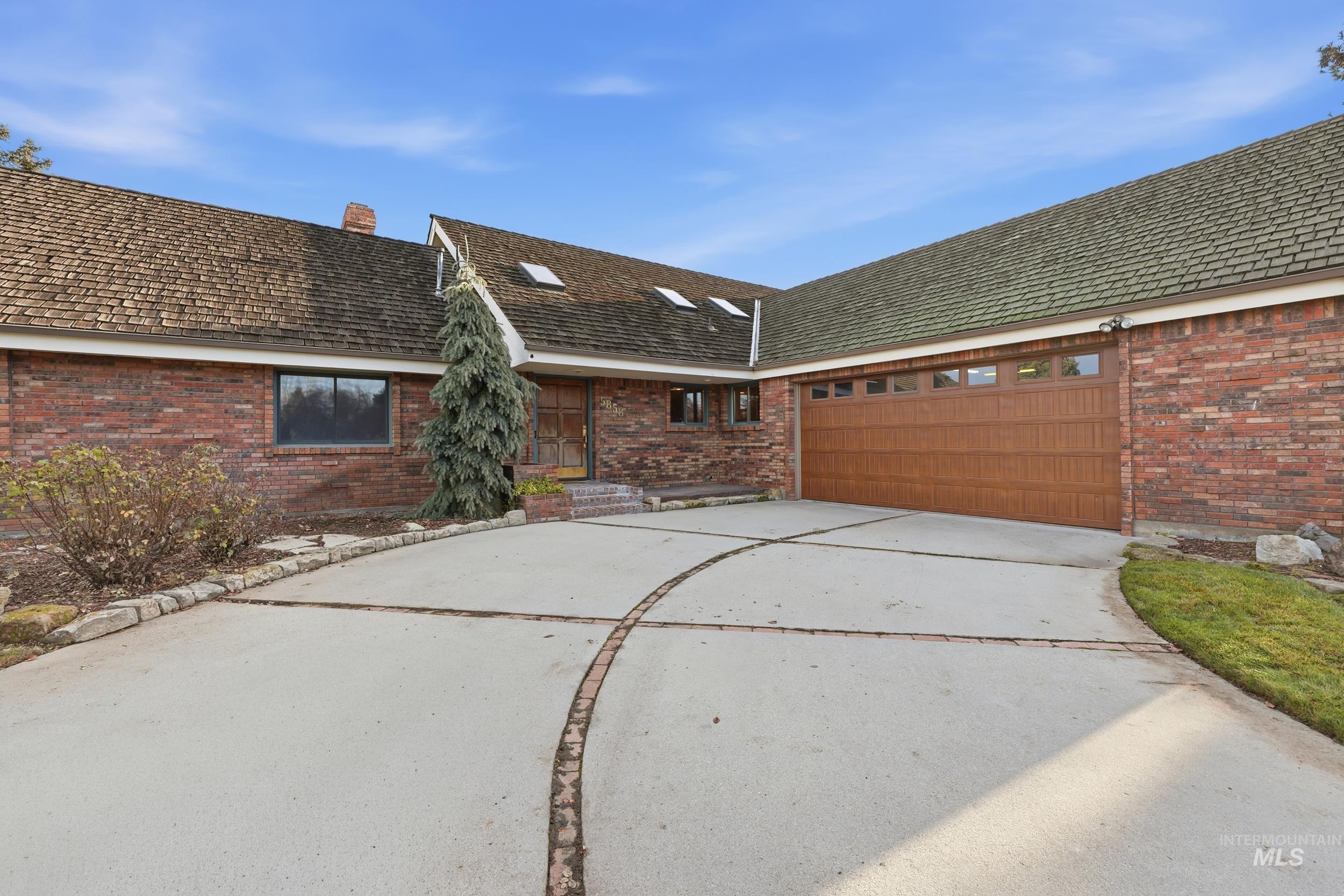 View of front facade with brick siding, driveway, a chimney, and a garage