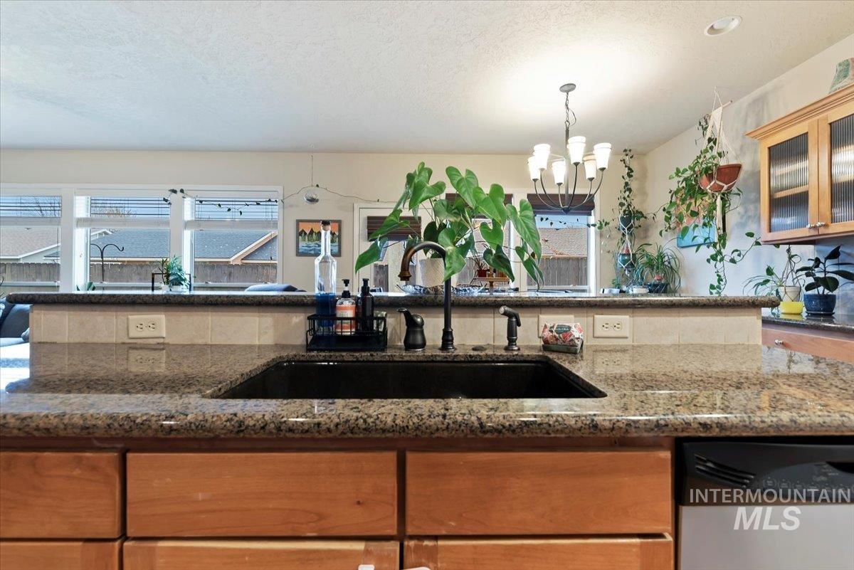 Kitchen featuring brown cabinets, dishwasher, dark stone countertops, glass insert cabinets, and a textured ceiling