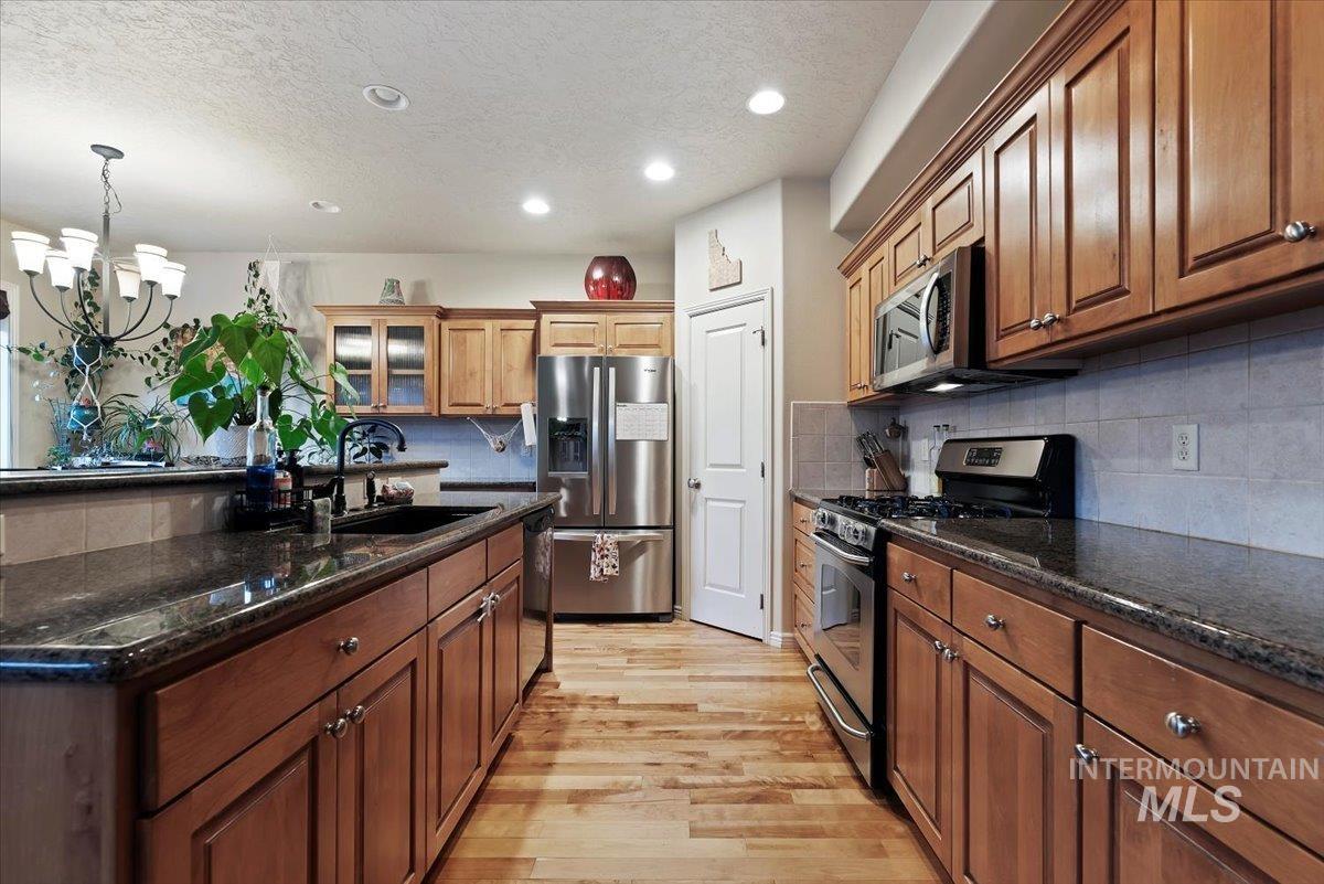 Kitchen featuring stainless steel appliances, dark stone countertops, glass insert cabinets, a textured ceiling, and light wood finished floors