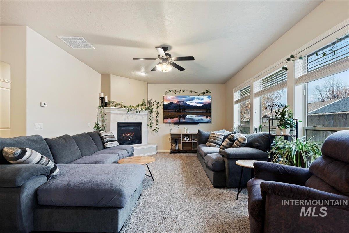 Living room with a glass covered fireplace, carpet flooring, and ceiling fan