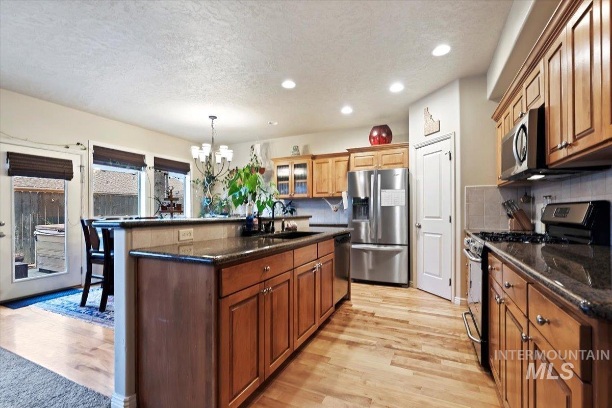 Kitchen featuring appliances with stainless steel finishes, a textured ceiling, glass insert cabinets, a kitchen island with sink, and light wood-type flooring