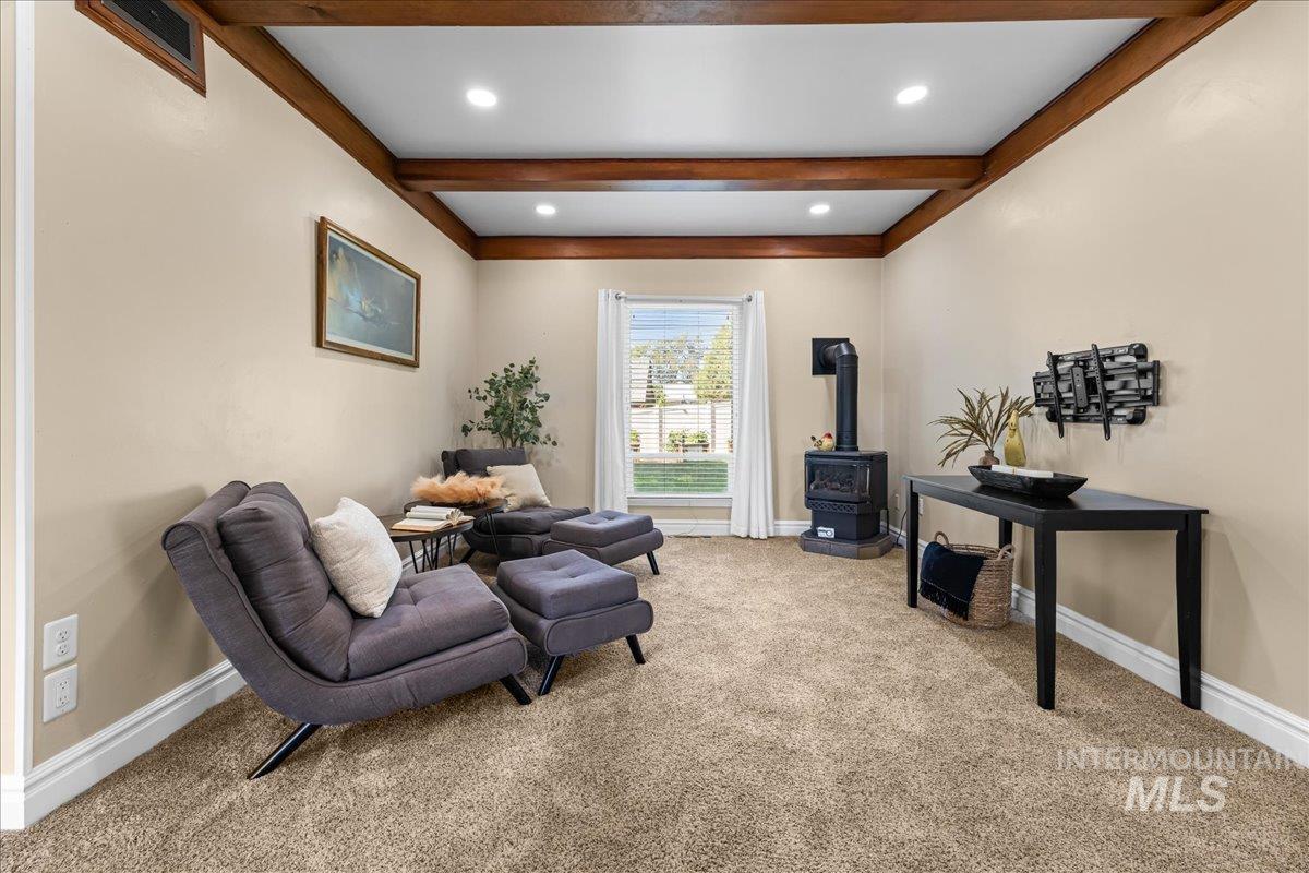 Living area with a wood stove, light colored carpet, beamed ceiling, and recessed lighting