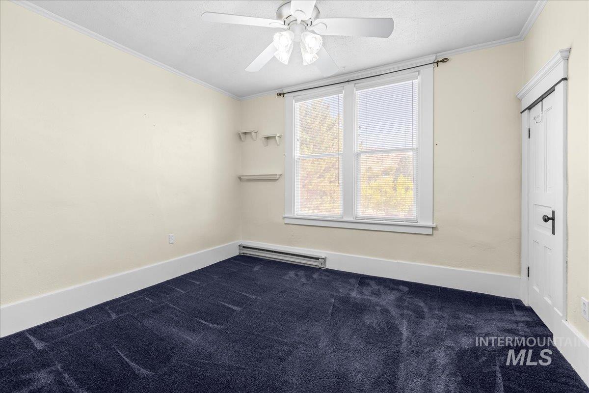Room with crown molding, dark carpet, baseboard heating, a textured ceiling, and ceiling fan