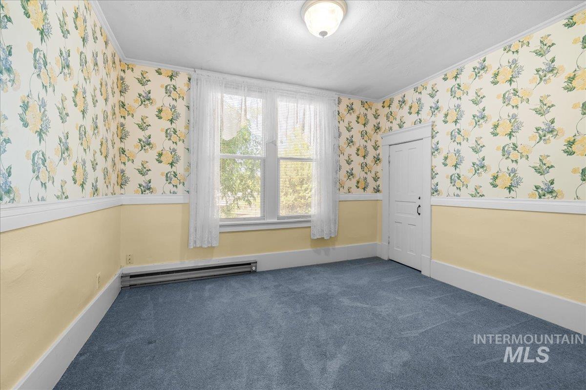 Spare bedroom with wallpapered walls, dark carpet, ornamental molding, a textured ceiling, and a baseboard heating unit