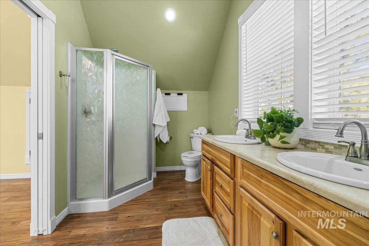 Full bathroom featuring a shower stall, dark wood-style floors, vaulted ceiling, double vanity, and recessed lighting