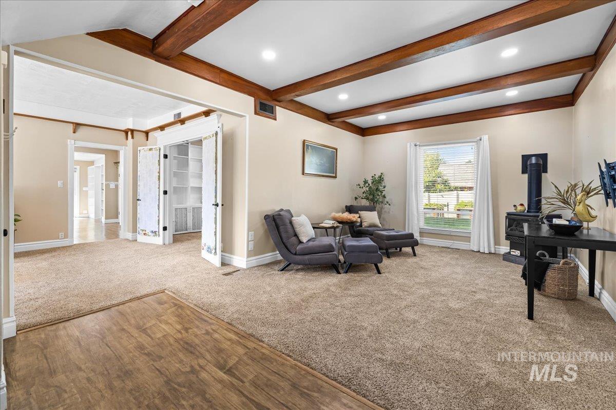Living area featuring carpet flooring, beamed ceiling, a wood stove, and recessed lighting