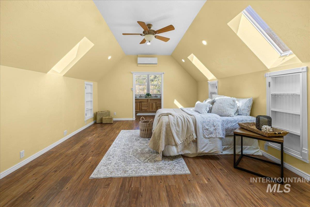 Bedroom featuring a skylight, lofted ceiling, dark wood-style flooring and a ceiling fan.