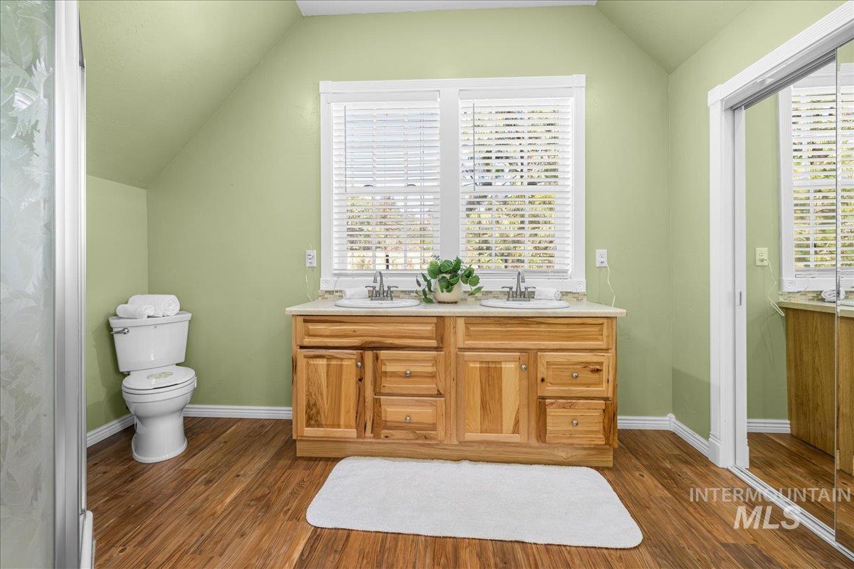 Bathroom with vaulted ceiling, double vanity, and dark wood-style floors