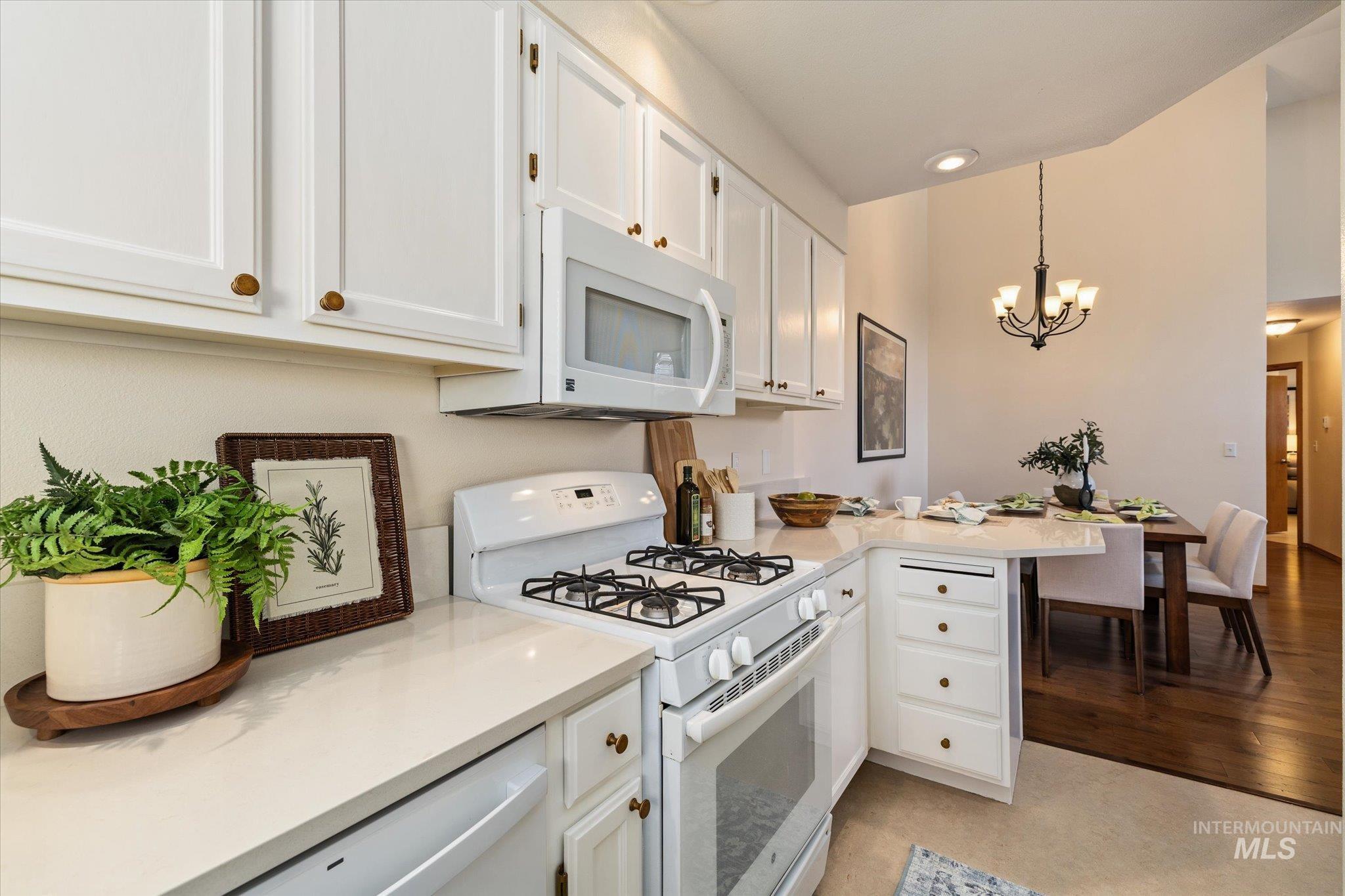 Kitchen with white appliances, white cabinets, a peninsula, a chandelier, and light stone counters