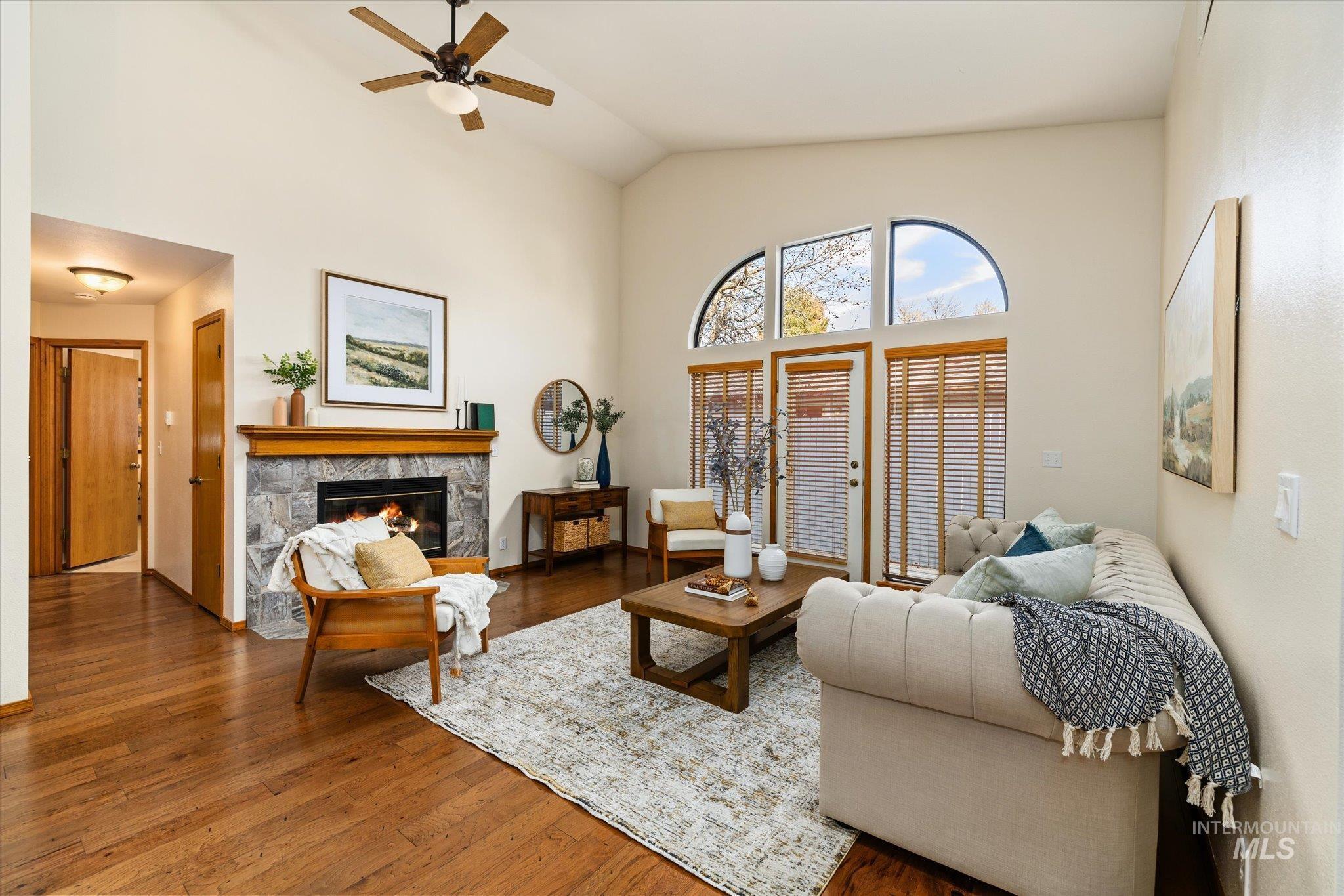Living room with a stone fireplace, a ceiling fan, wood finished floors, and vaulted ceiling