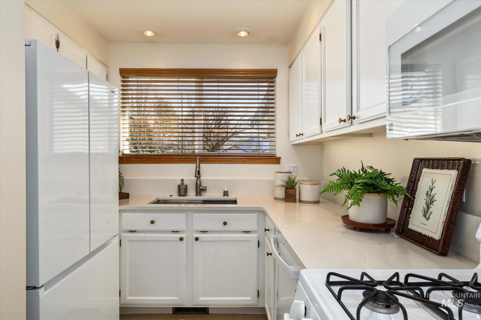 Kitchen with white appliances, white cabinets, recessed lighting, and light stone counters
