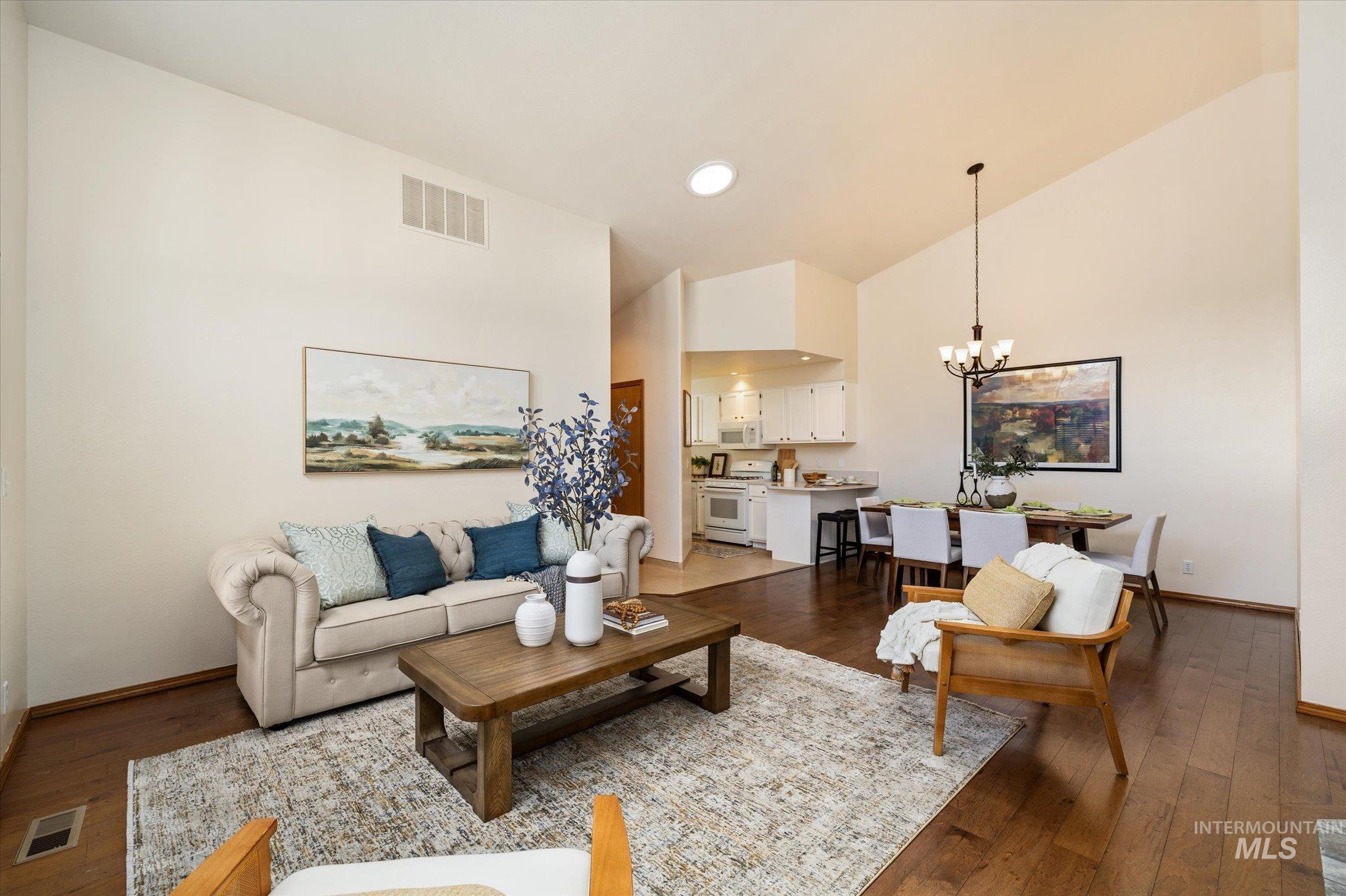 Living room with dark wood-type flooring, a chandelier, and lofted ceiling