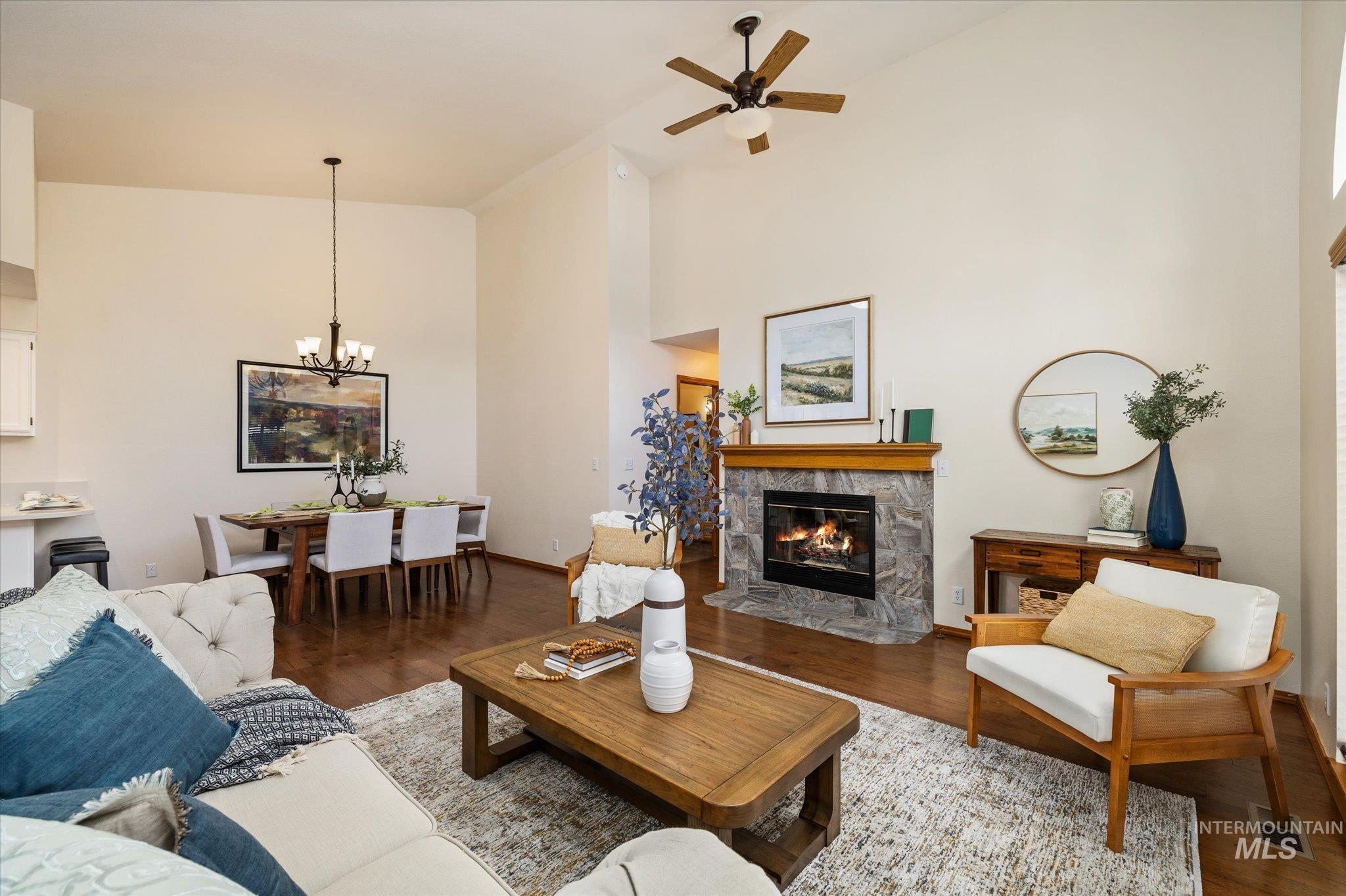 Living area with a high ceiling, wood finished floors, a ceiling fan, a tiled fireplace, and suspended lighting