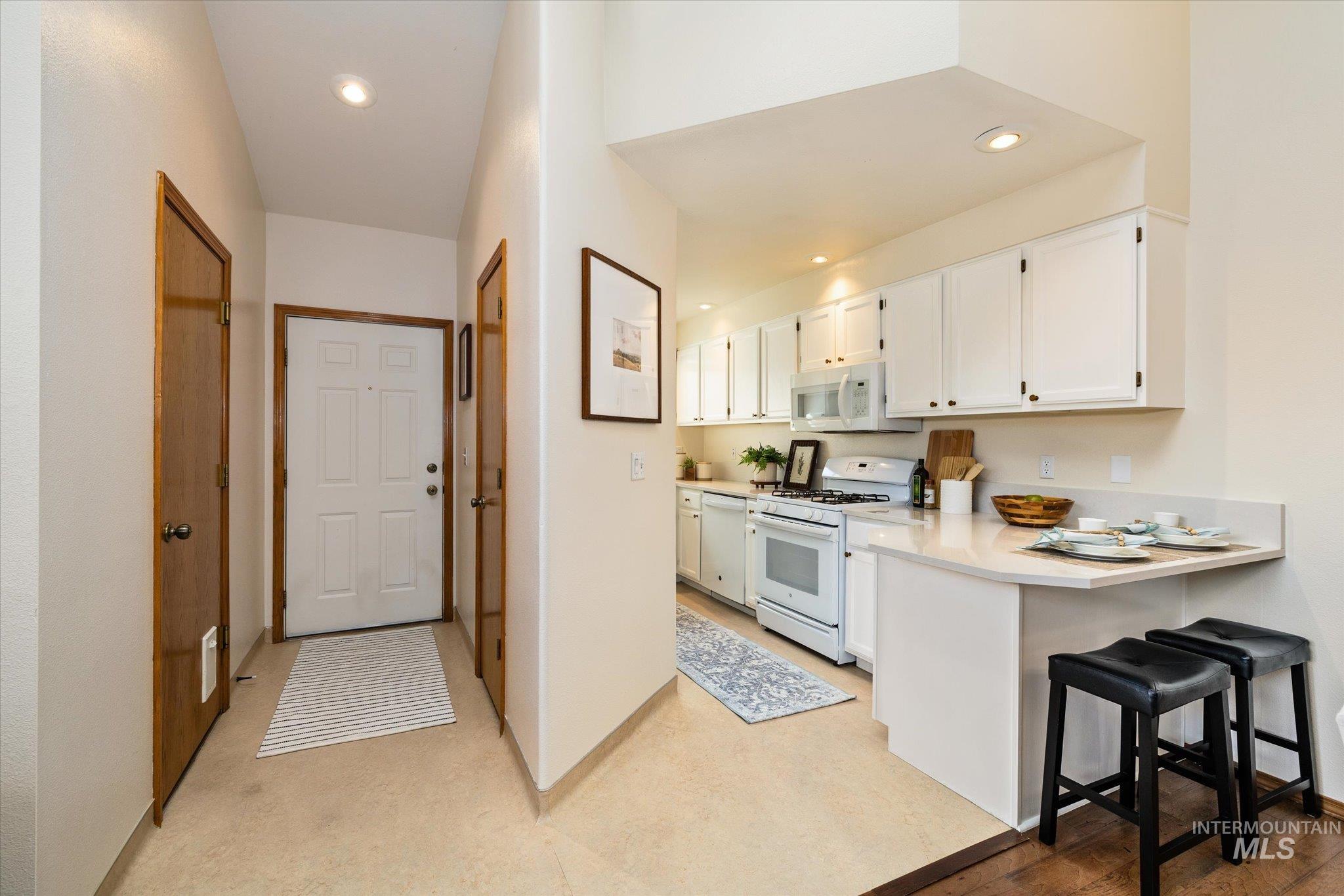 Kitchen featuring white appliances, white cabinets, a kitchen bar, recessed lighting, and a peninsula