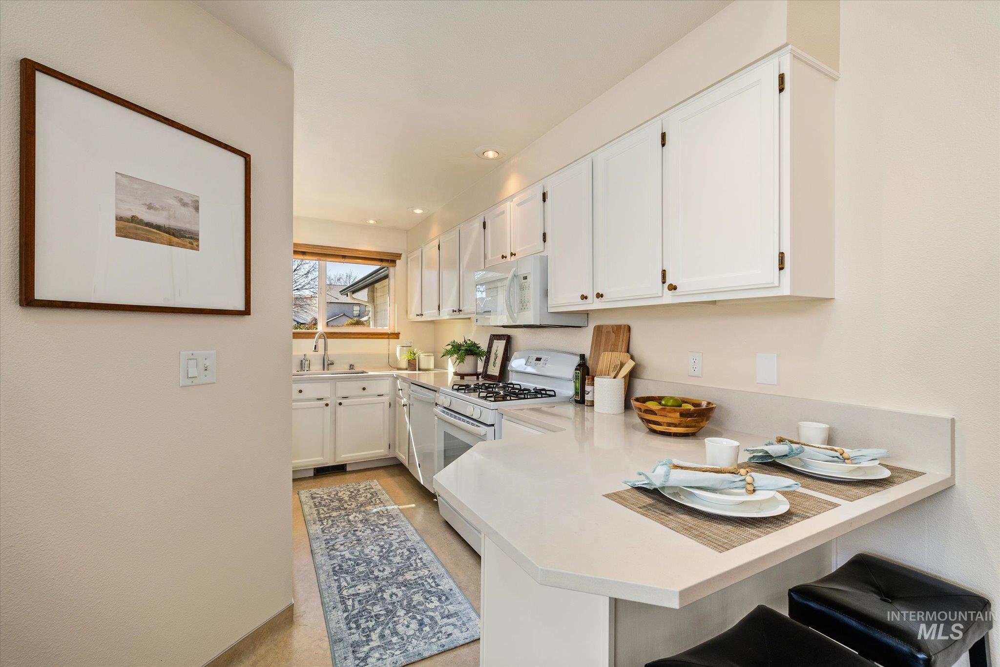 Kitchen featuring white cabinetry, white appliances, light countertops, a kitchen breakfast bar, and a peninsula