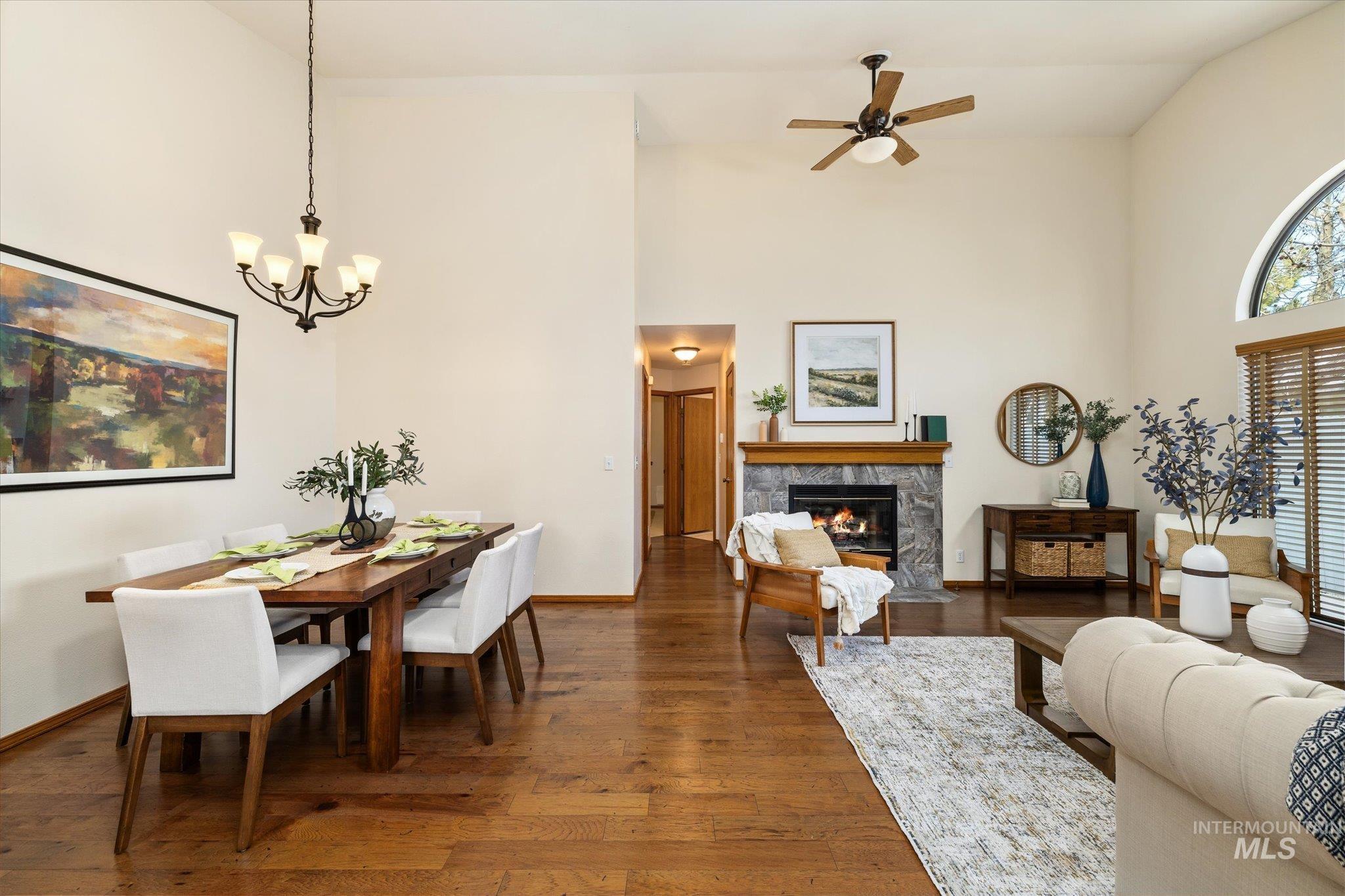Dining space featuring a high end fireplace, hardwood / wood-style flooring, ceiling fan, a chandelier, and vaulted ceiling