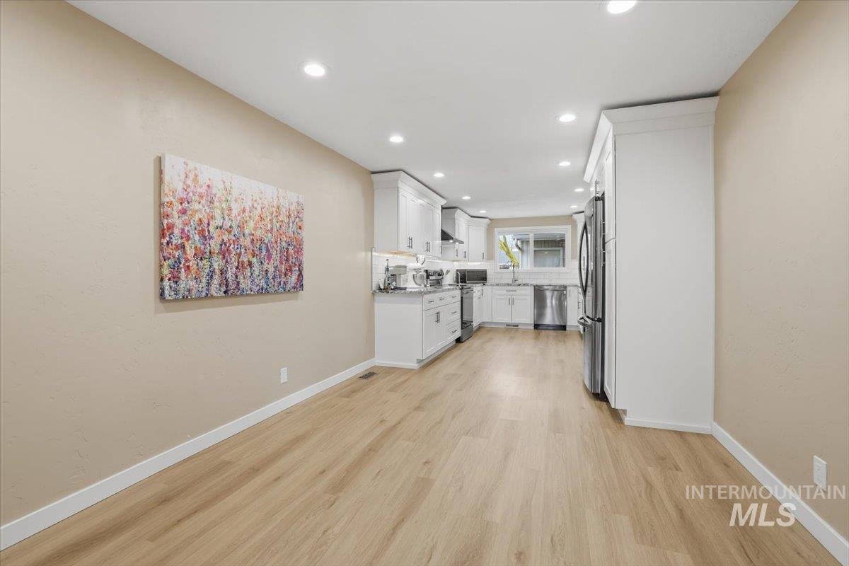 Kitchen featuring white cabinets, recessed lighting, stainless steel appliances, light wood finished floors, and wall chimney range hood