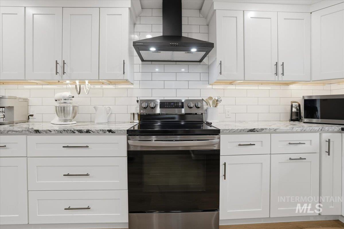 Kitchen featuring appliances with stainless steel finishes, wall chimney exhaust hood, light stone countertops, and white cabinets