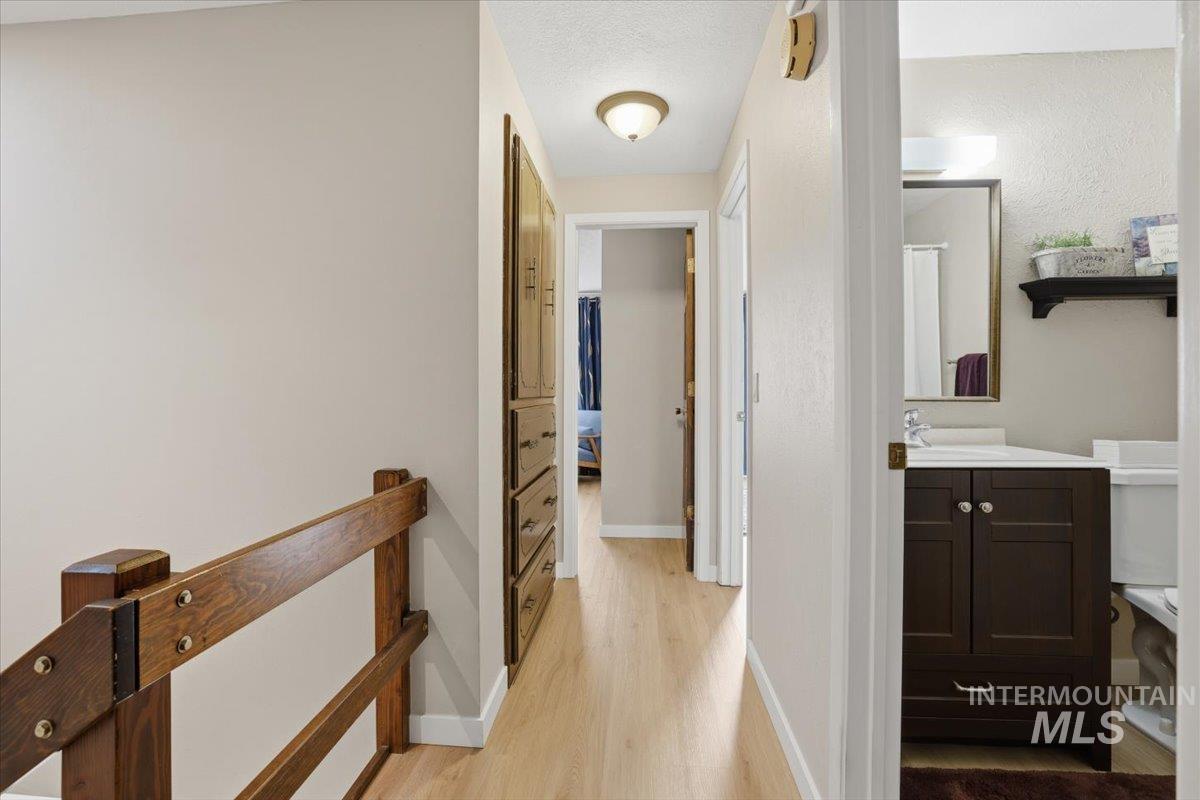 Corridor featuring light wood-style floors, an upstairs landing, and a textured ceiling