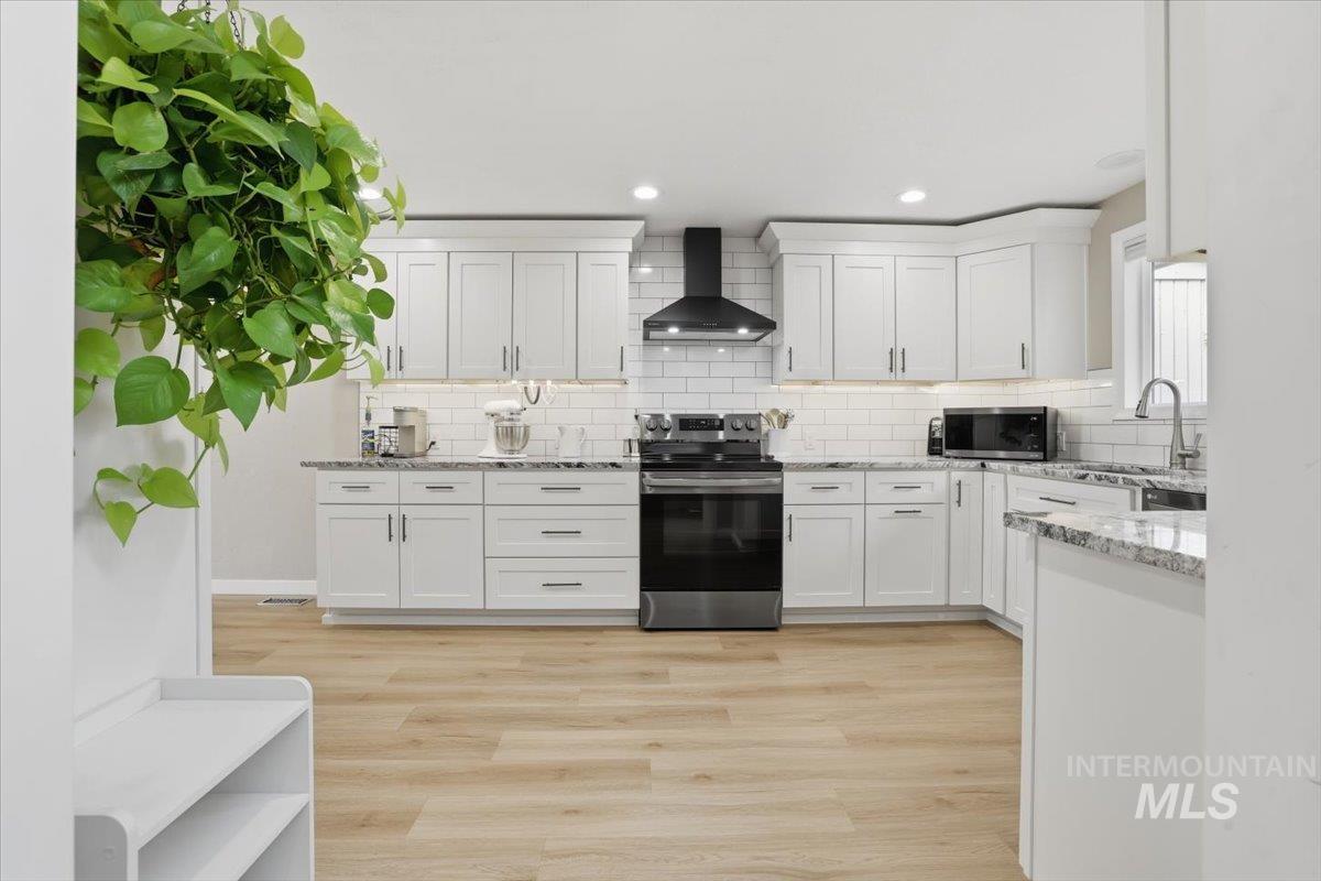 Kitchen featuring appliances with stainless steel finishes, white cabinets, wall chimney exhaust hood, light stone counters, and light wood-type flooring