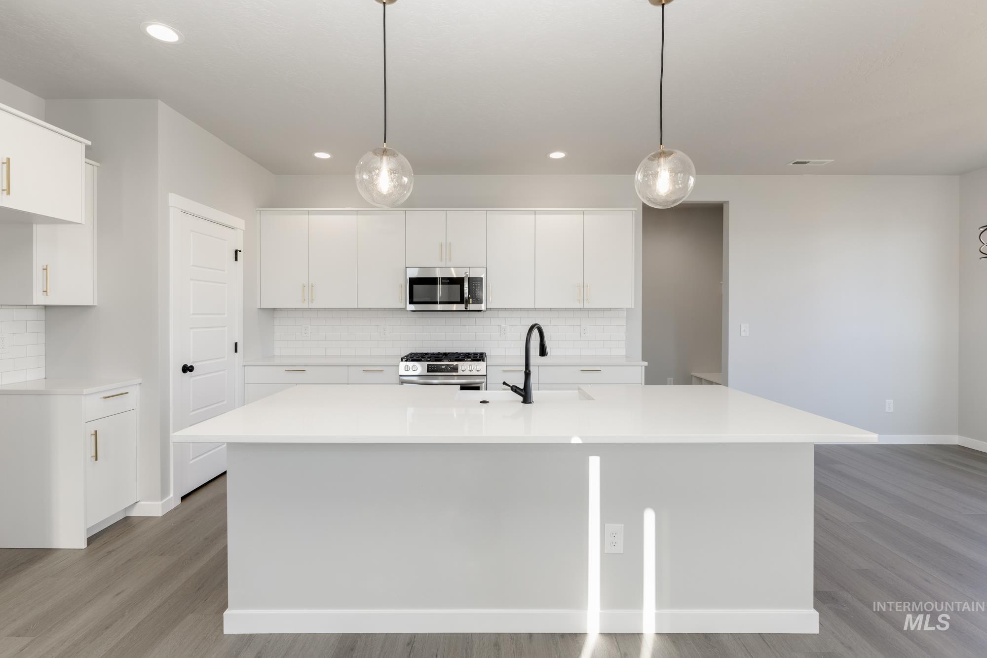 Kitchen with tasteful backsplash, a center island with sink, light wood finished floors, white cabinetry, and recessed lighting