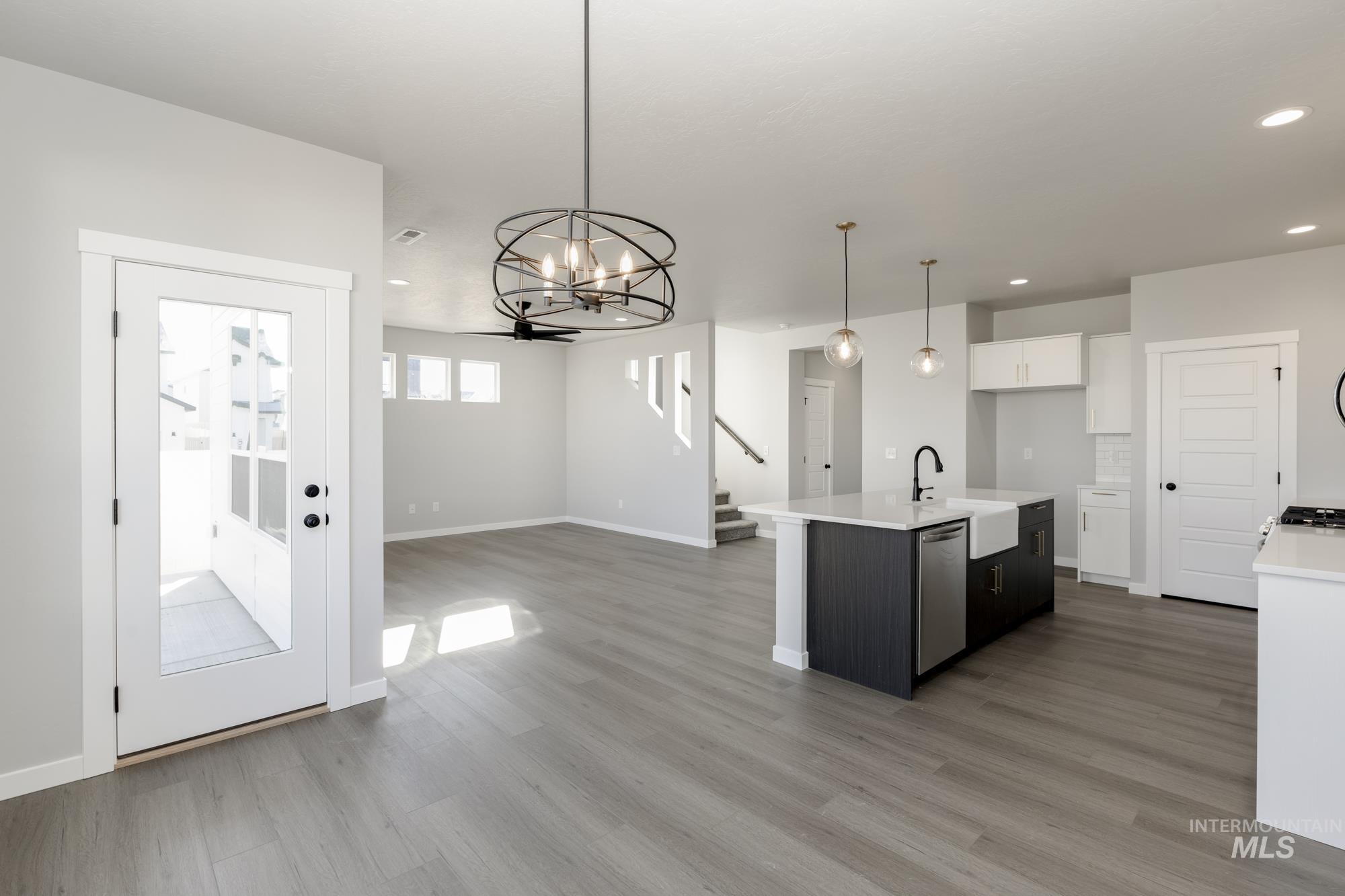 Kitchen with a center island with sink, a chandelier, hanging light fixtures, light stone counters, and open floor plan